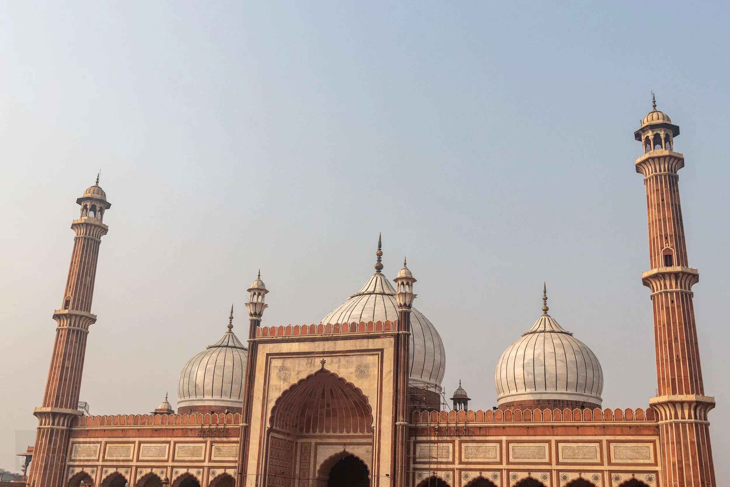 A large tan and brown mosque featuring three gray domes, Delhi, India.
