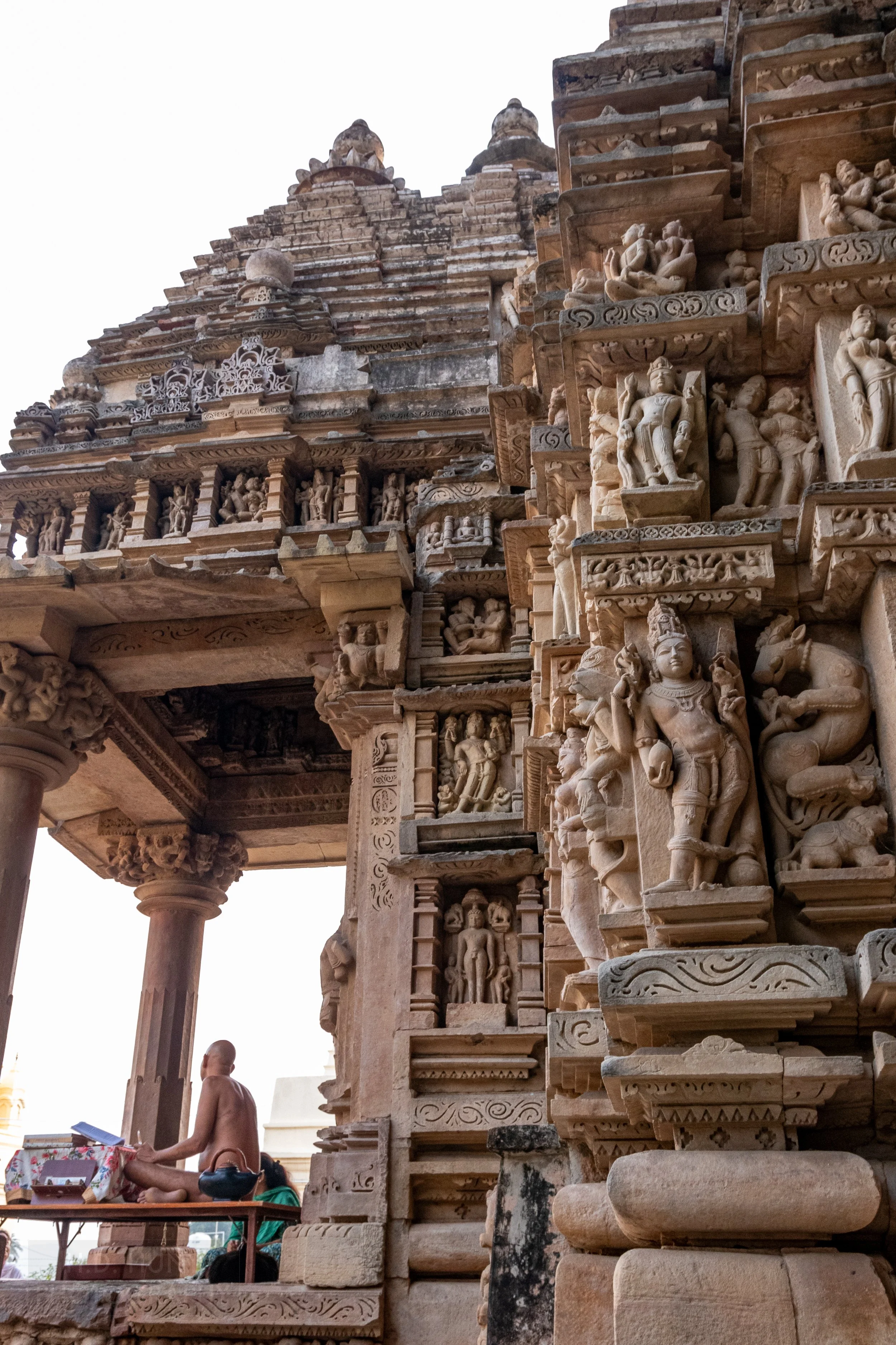 A close-up of the stone figures on Parshvanatha, Khajuraho, India with an unclothed man meditating nearby.