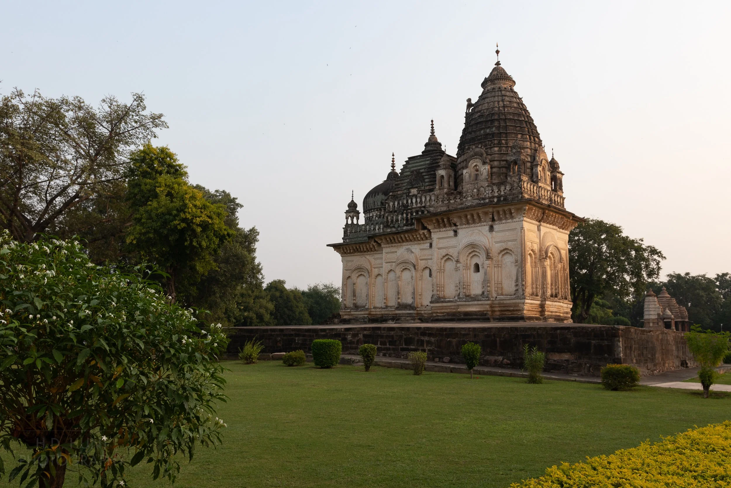 The white and black Pratapeshwar Temple rises above manicured grass at the Khajuraho Group of Monuments, India.