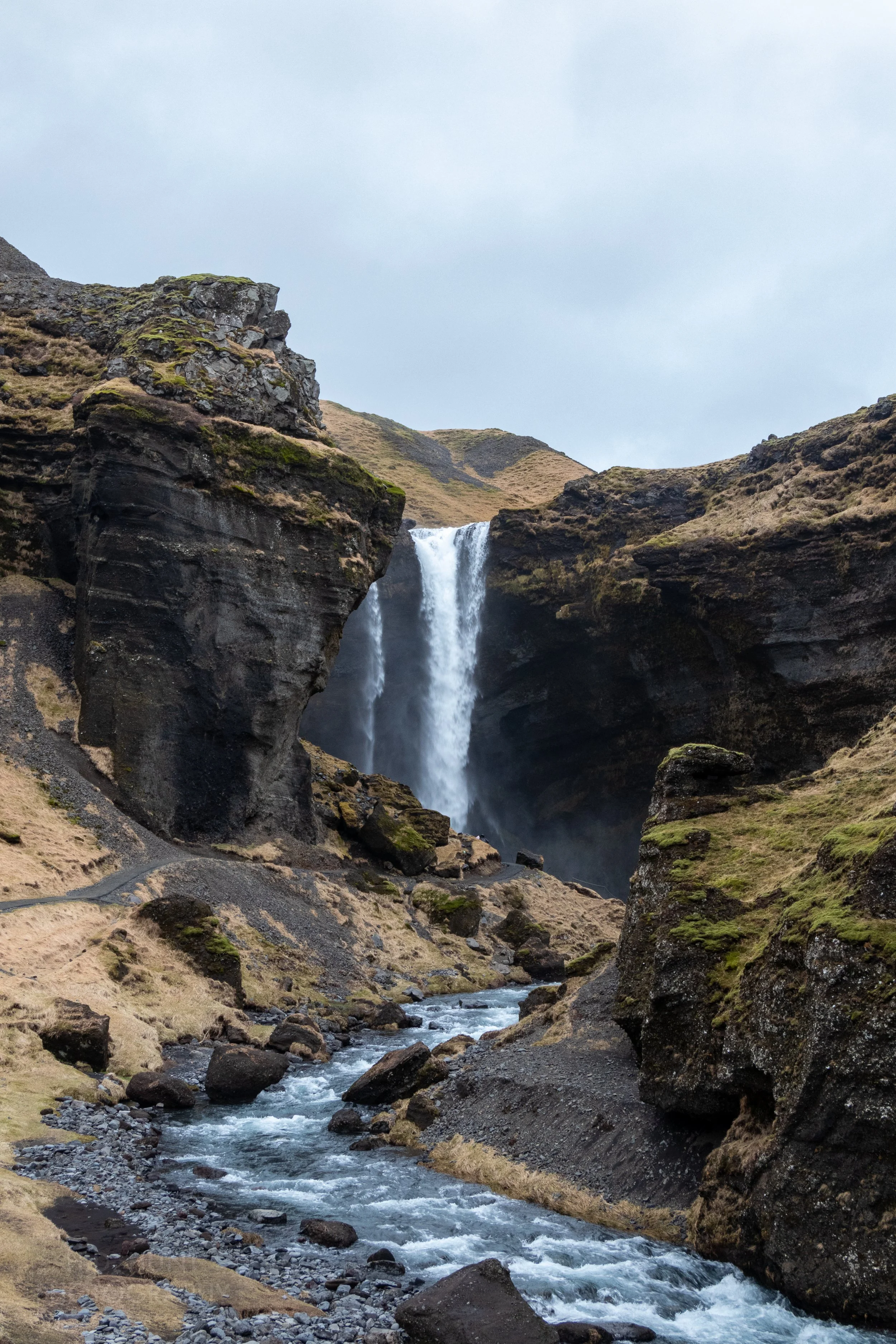 A waterfall sends water into a deep valley surrounded by tall black rock cliffs, Kvernufoss, Iceland.