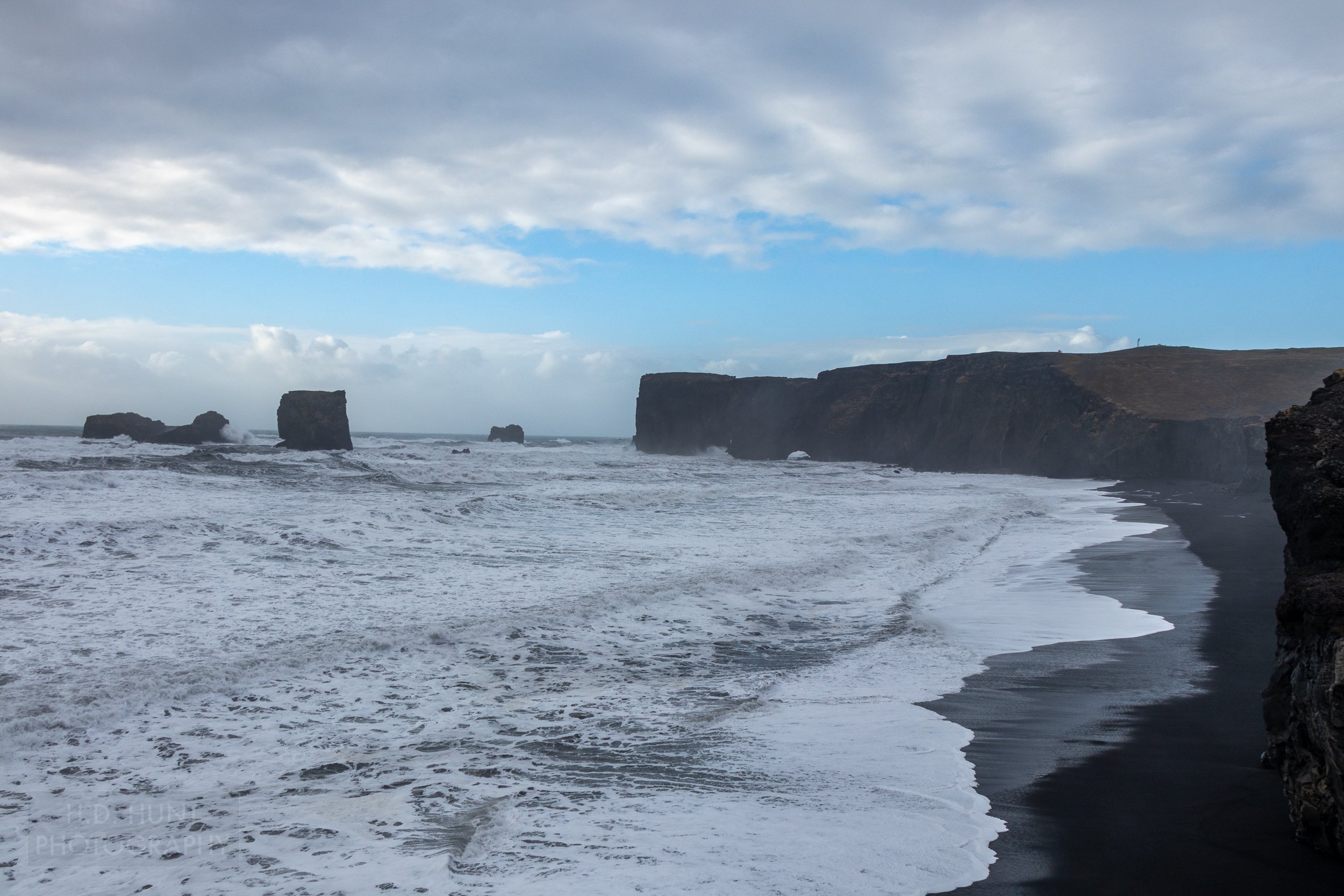 Tall black cliffs rise from the Atlantic Ocean against black sand beaches at Dyrhólaey, Iceland.