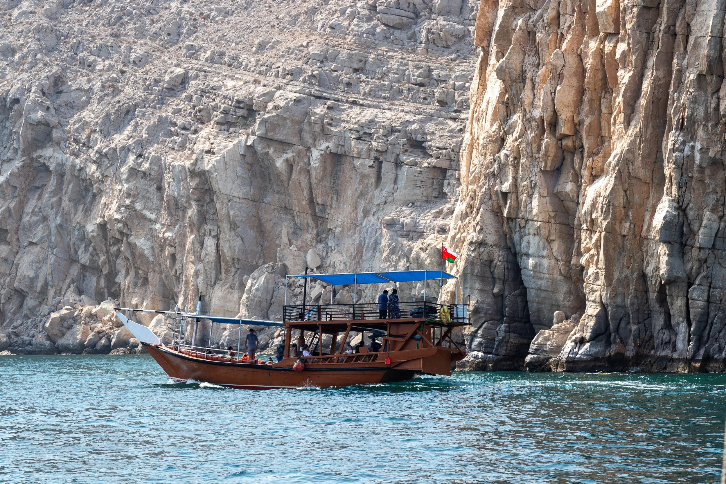A dhow boat passes close to the tall white cliffs of the Musandam Peninsula, Oman.
