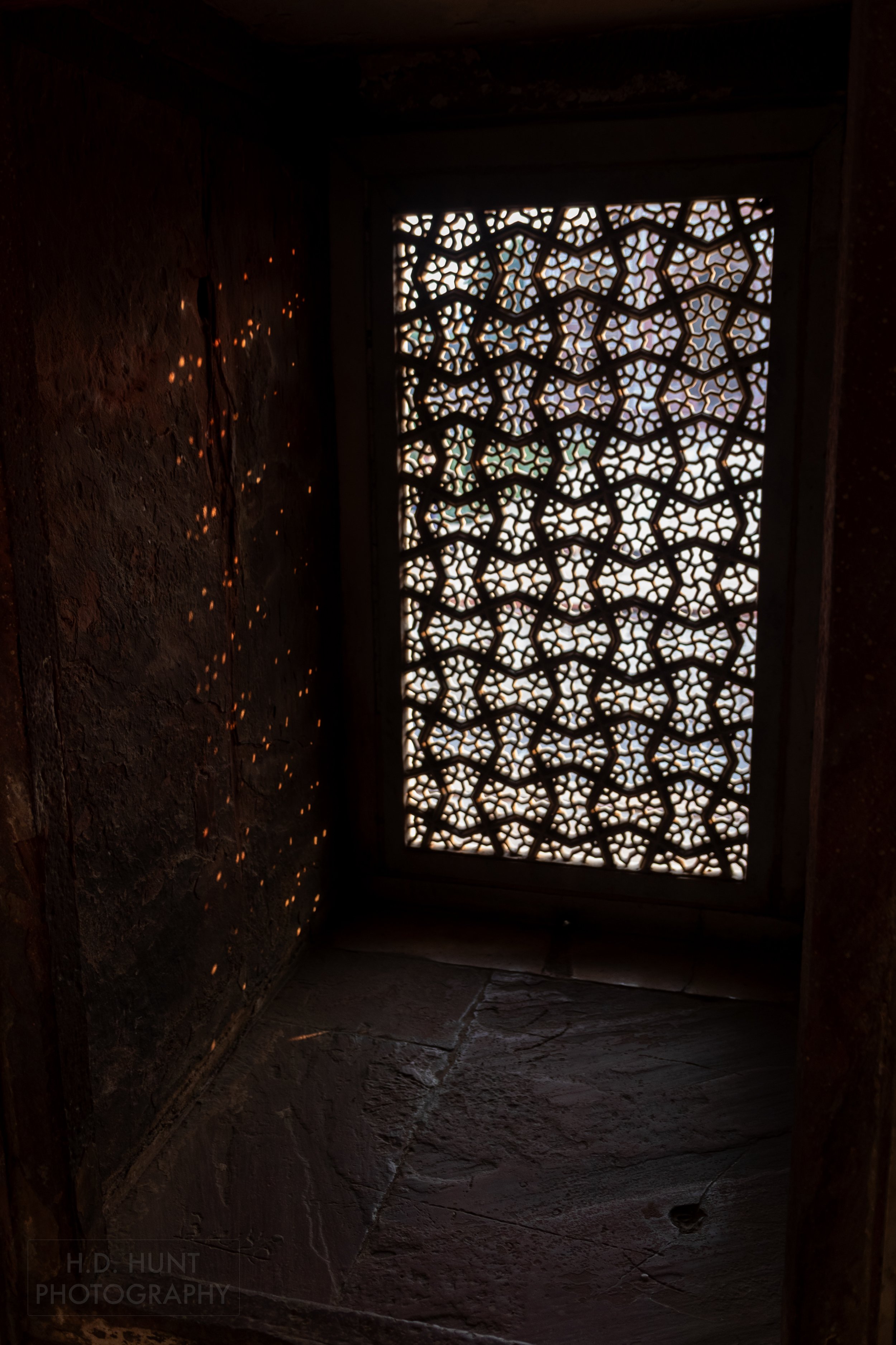 A delicately carved stone window screen allows dots of light through to beam onto a dark wall at the Tomb of I’timad-ud-Daulah, Agra, India.