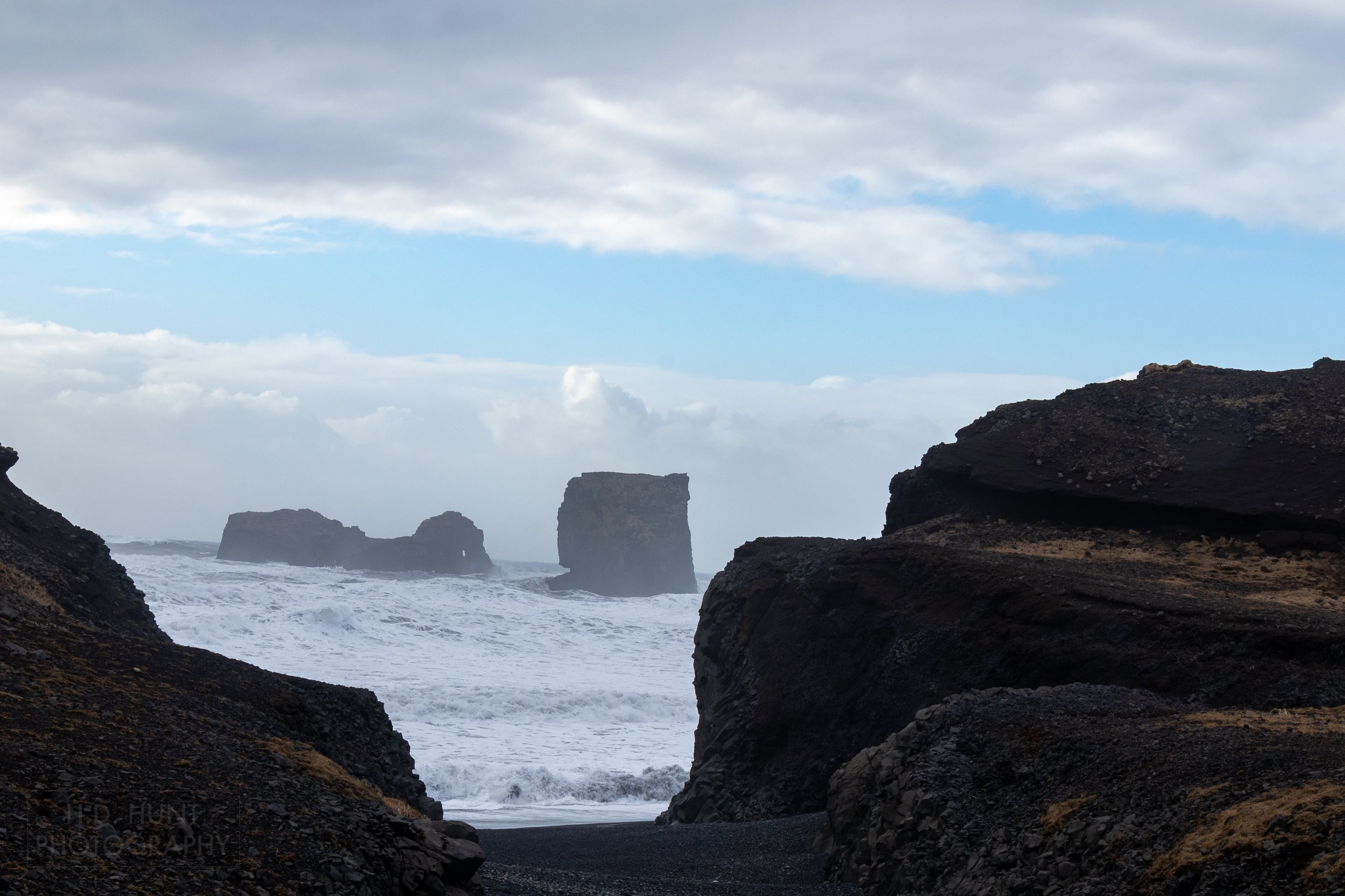 Large waves crash against rock pillars and coastal cliffs, Dyrhólaey, Iceland.