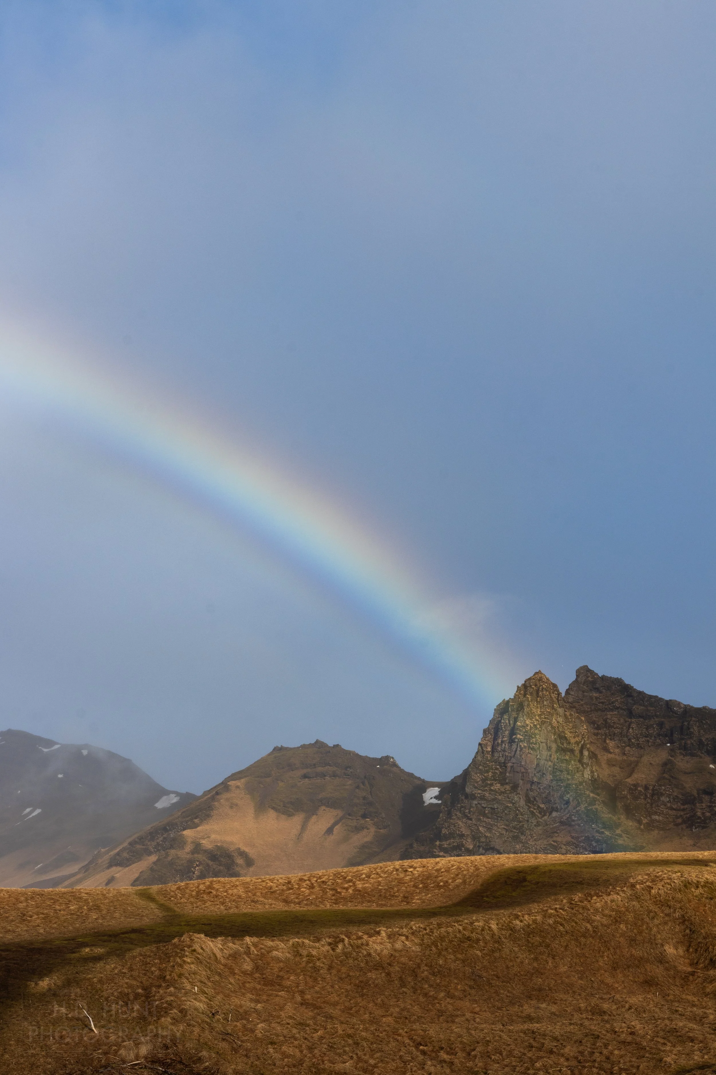 A rainbow forms over the brown grass surrounding Vík í Mýrdal, Iceland.