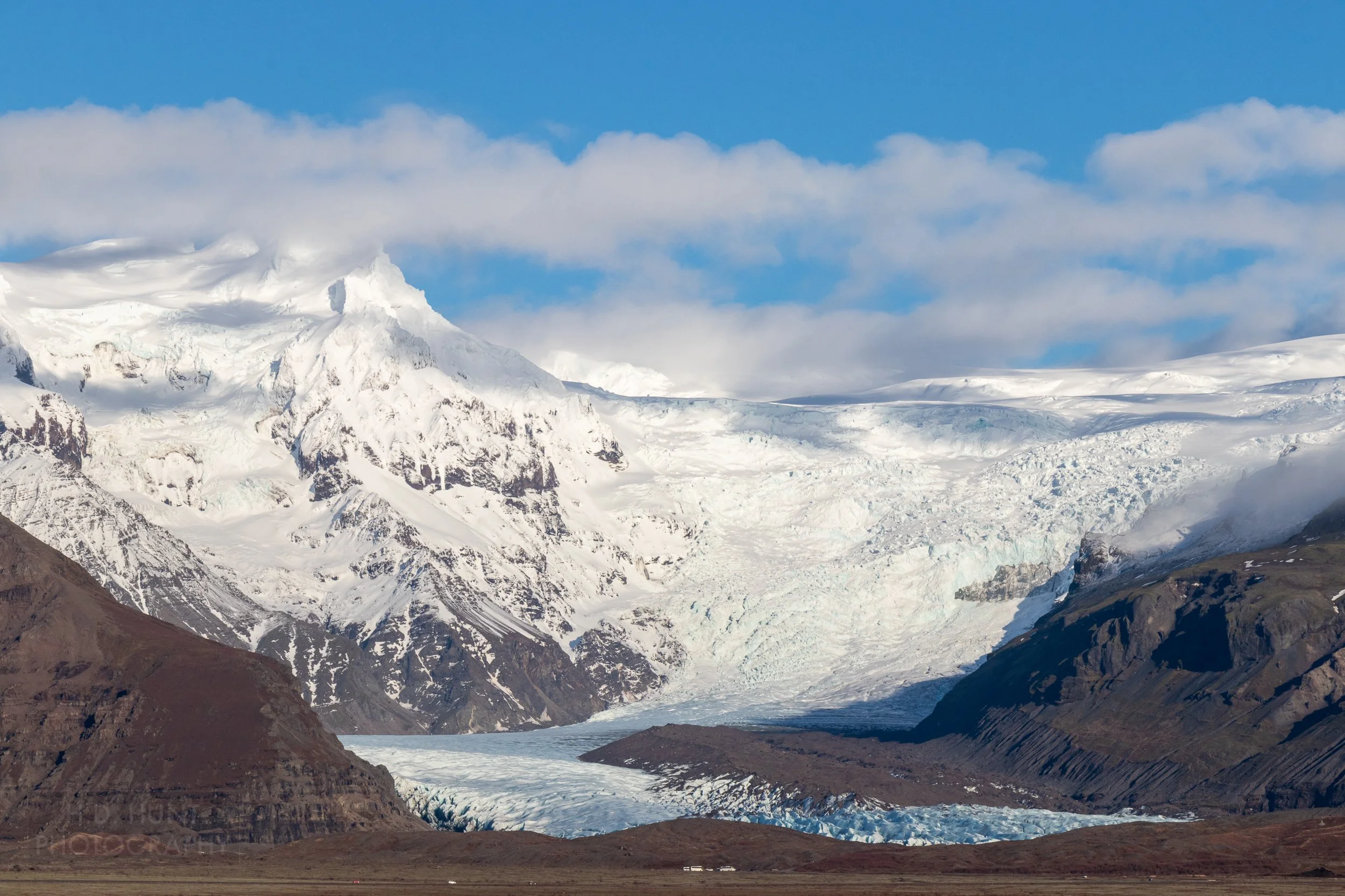 The Skeiðarárjökull glacier flows into a deep valley surrounded by dark rocky cliffs, Iceland.