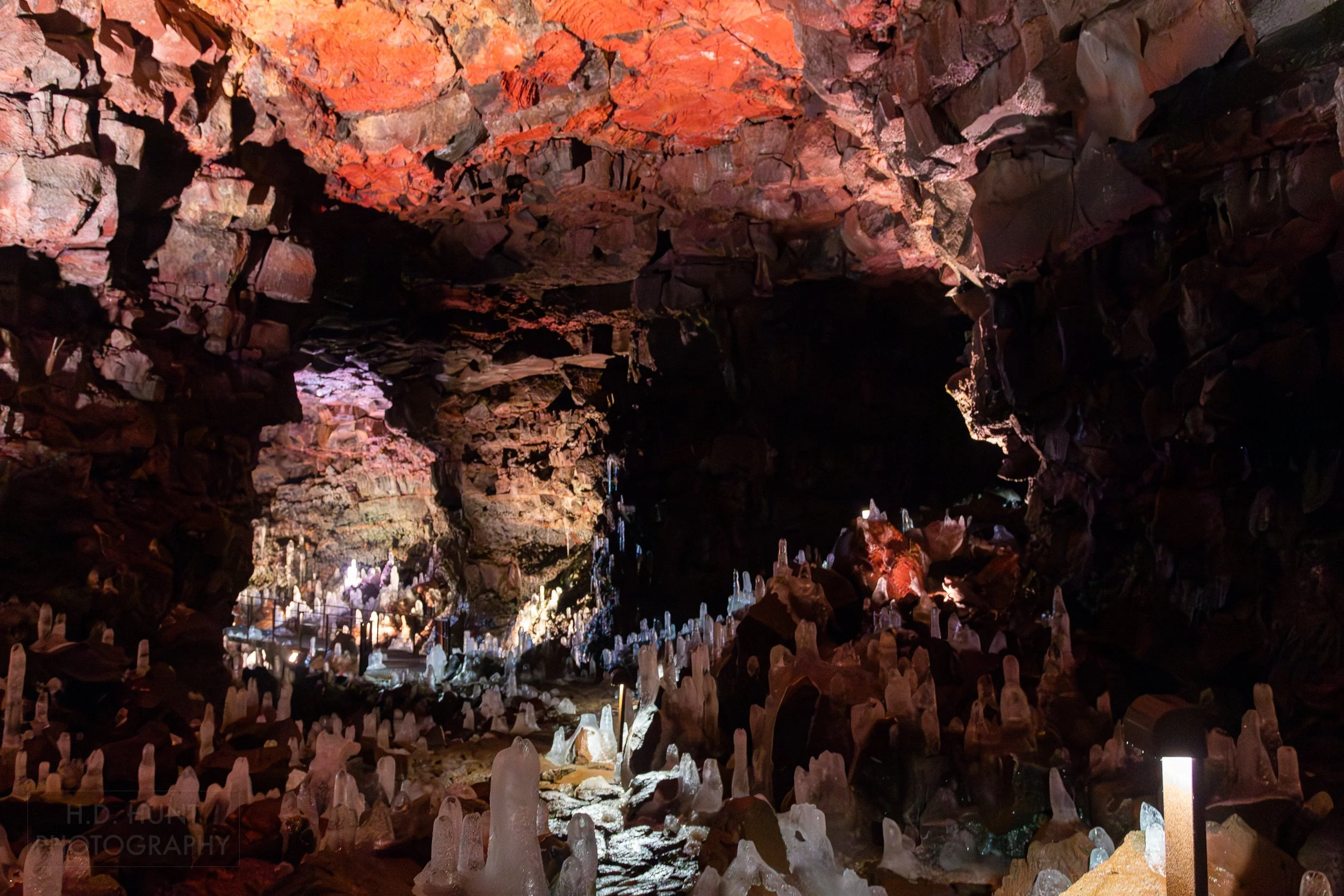 A long cavern with red and brown walls featuring ice columns on the floor is seen in the lava tube Raufarhólshellir, Iceland.