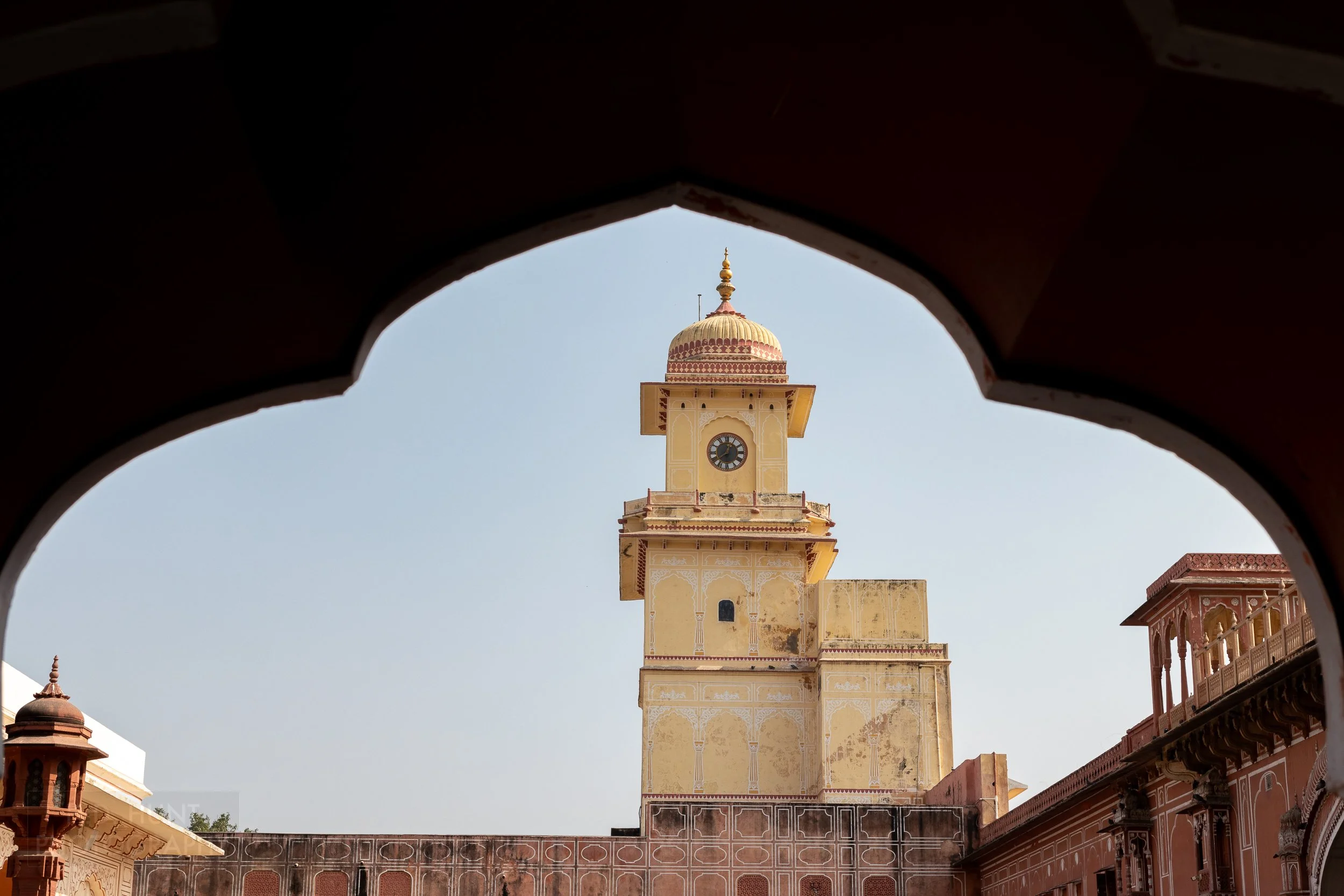 A tall yellow clocktower is seen through an arch, City Palace, Jaipur, India.
