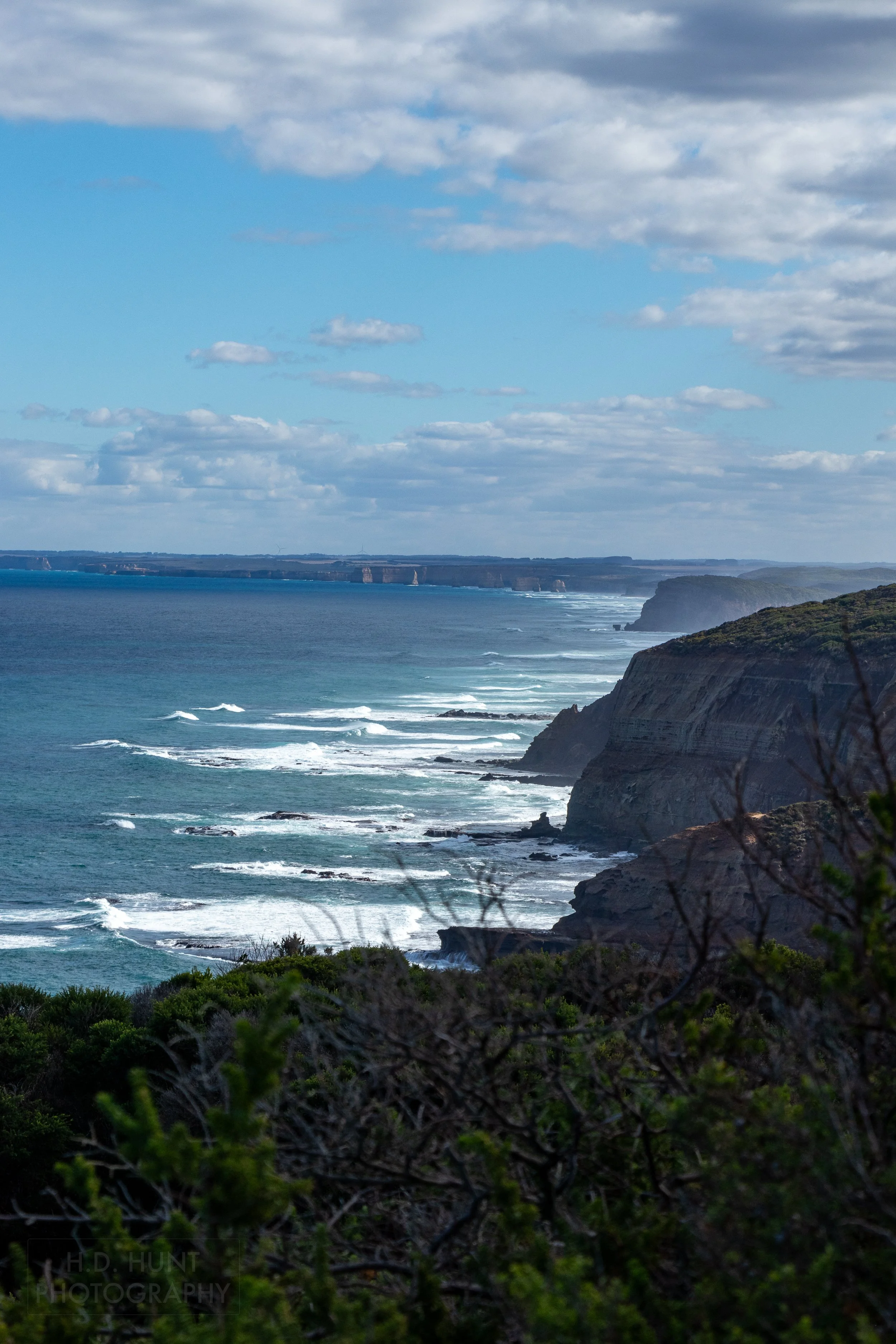 Far in the distance behind the blue ocean, the cliff spires of The Twelve Apostles can be seen along The Great Ocean Walk, Victoria, Australia.