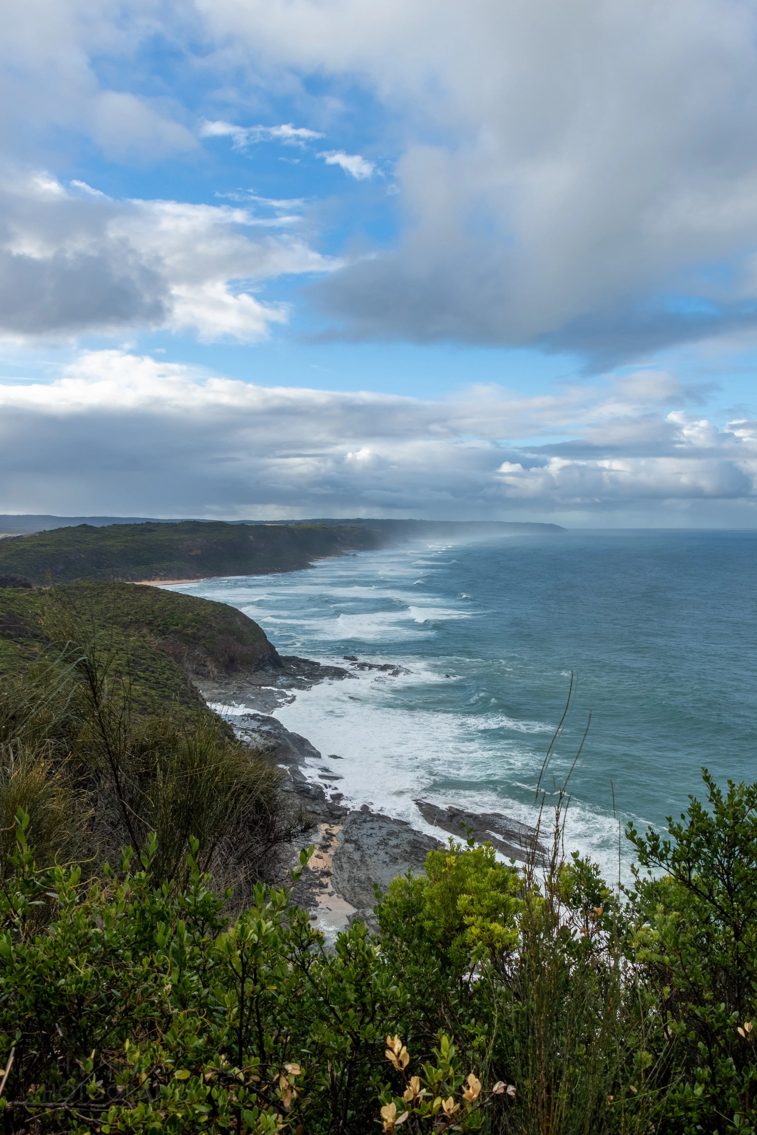 Waves crash into tall cliffs beneath green bushes near Johanna, Victoria, Australia along The Great Ocean Walk.