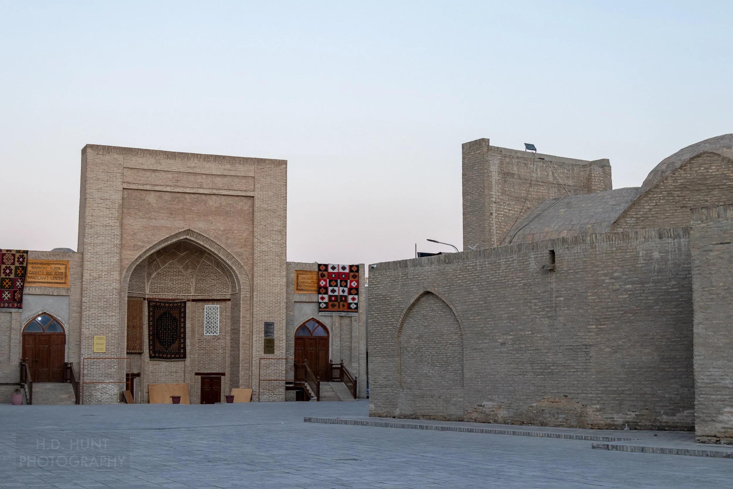 A carpet and handicraft business with rugs hanging outside can be seen in a square in Bukhara, Uzbekistan.