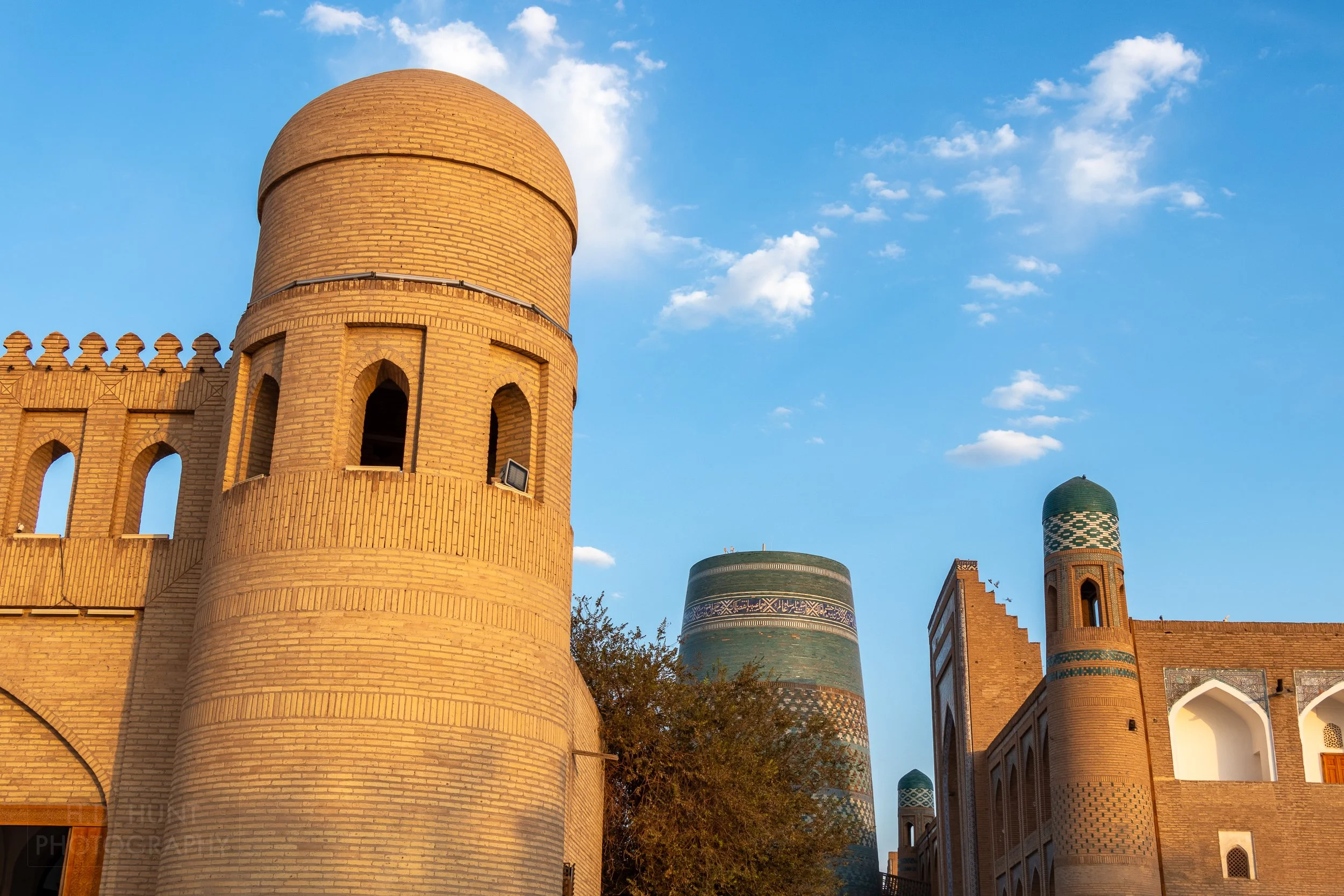 A tower of Khiva's Ota Gate is seen in the foreground, with the blue-tiled Kalta Minor in the background.