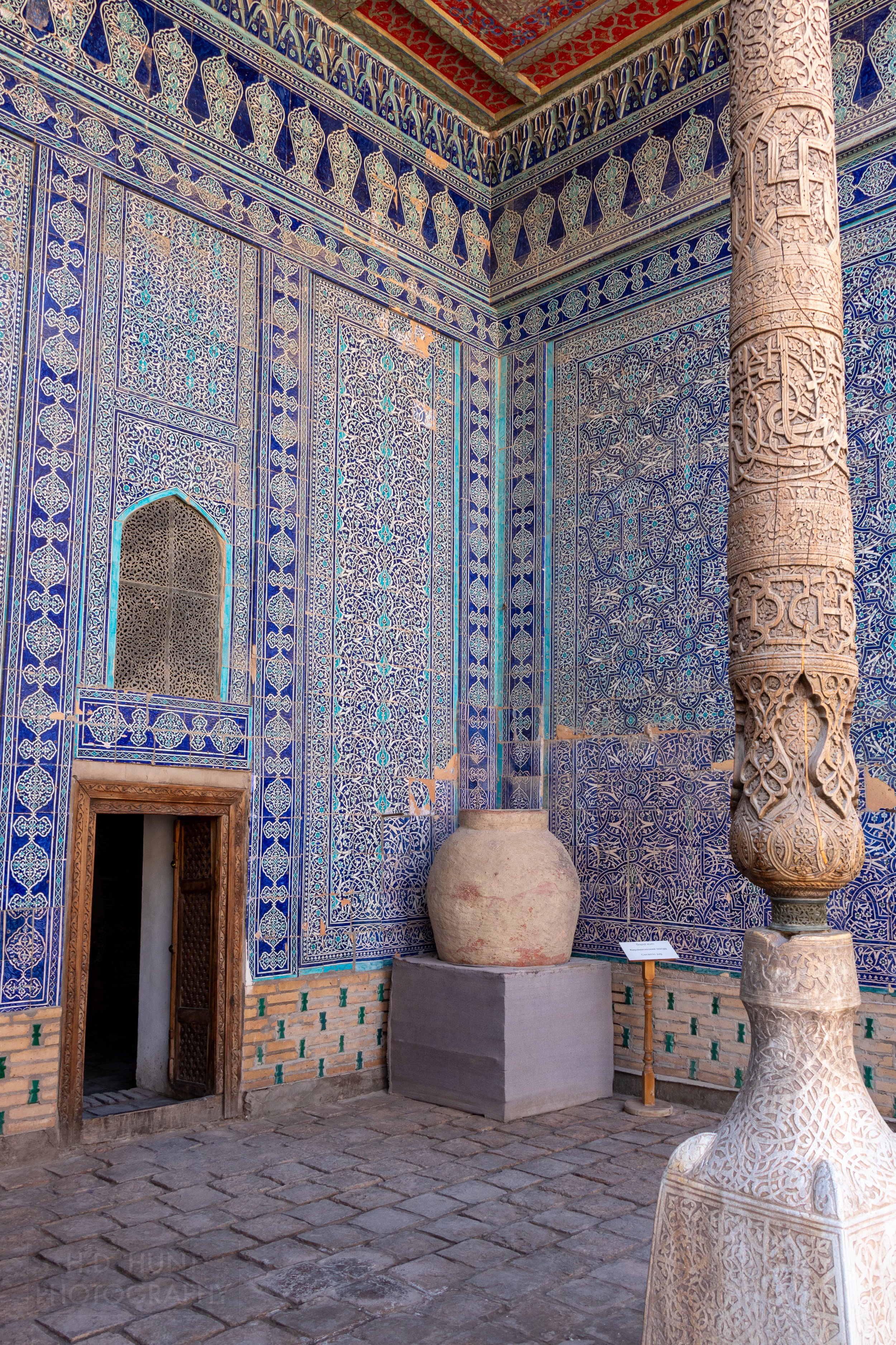 A large clay urn sits in the corner of a portico lined with intricate blue and white tiles, Toshhovli Palace, Khiva, Uzbekistan.