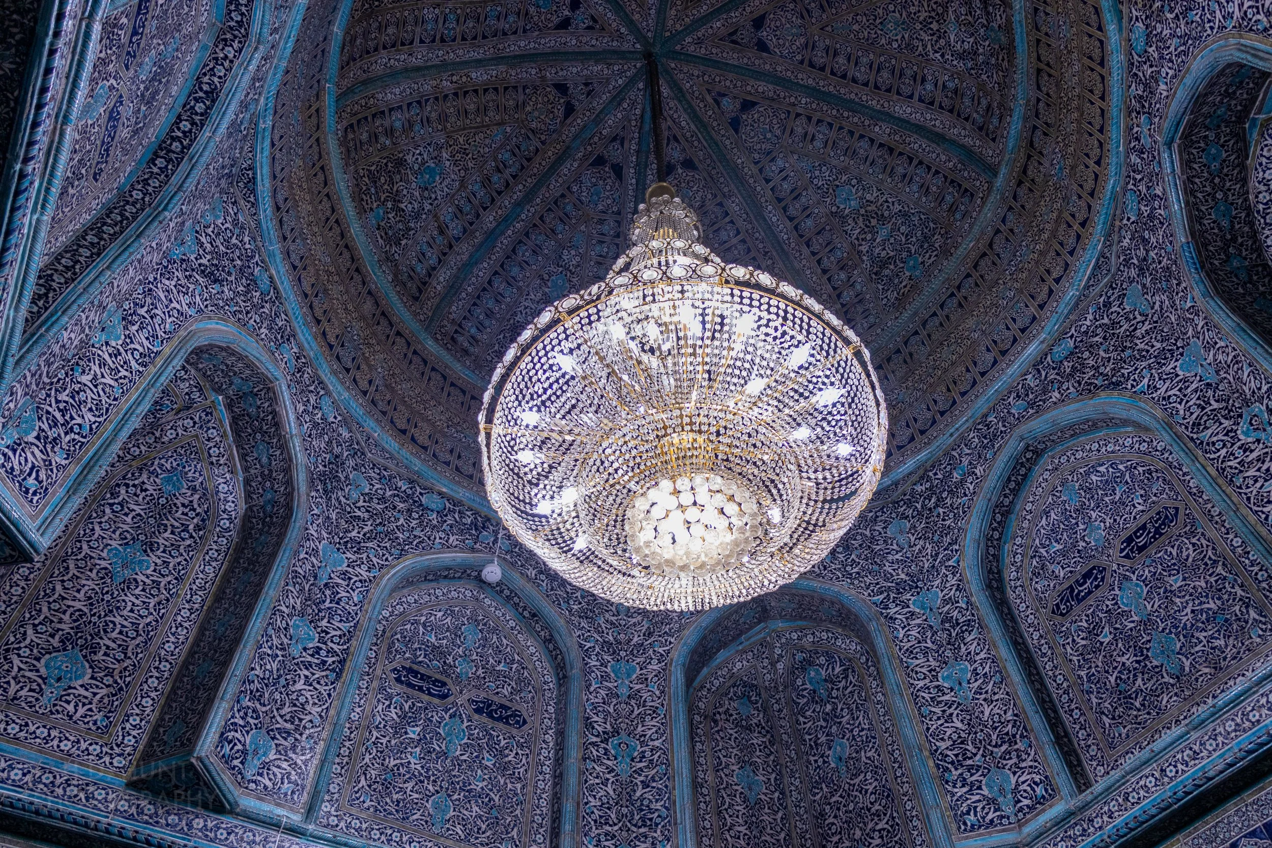 An elegant chandelier hangs from a large dome within the Pahlavan Mahmoud Mausoleum in Khiva, Uzbekistan.