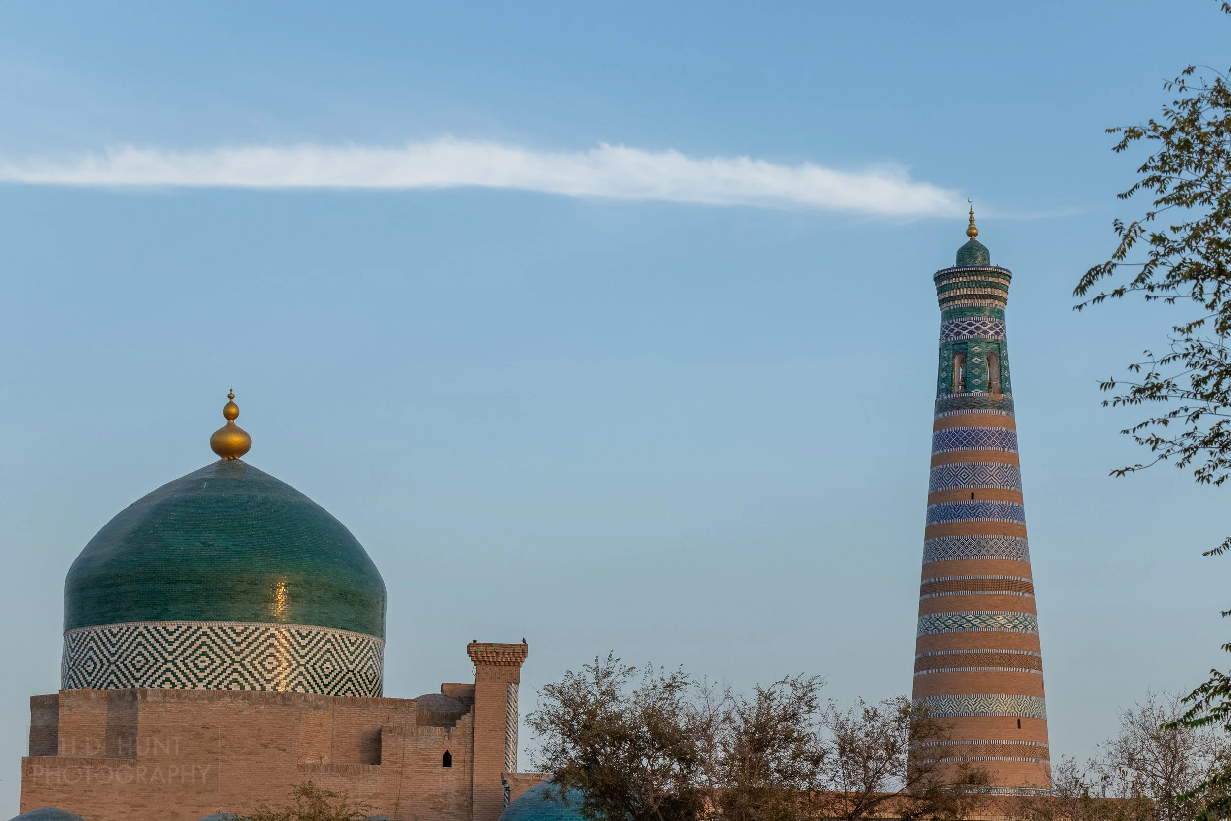 A green domed mausoleum and a tall minaret tower over Khiva, Uzbekistan.