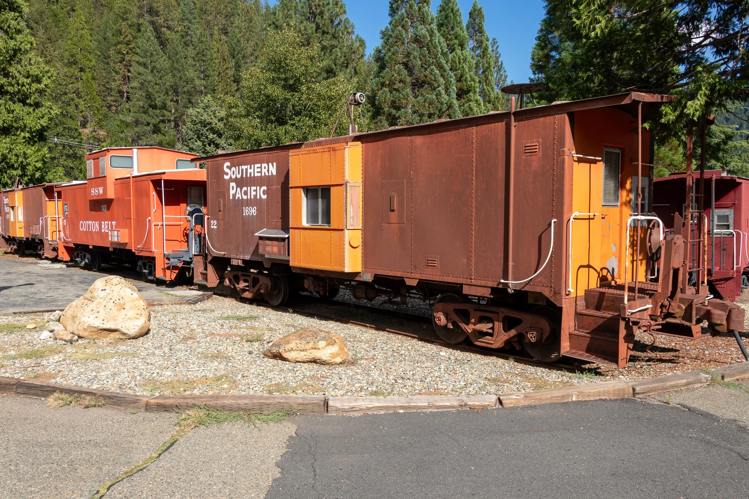 Multiple red and orange railroad cars are parked along a roadway at the Jubilee Railroad Wilderness Lodge, Dunsmuir, California, United States.