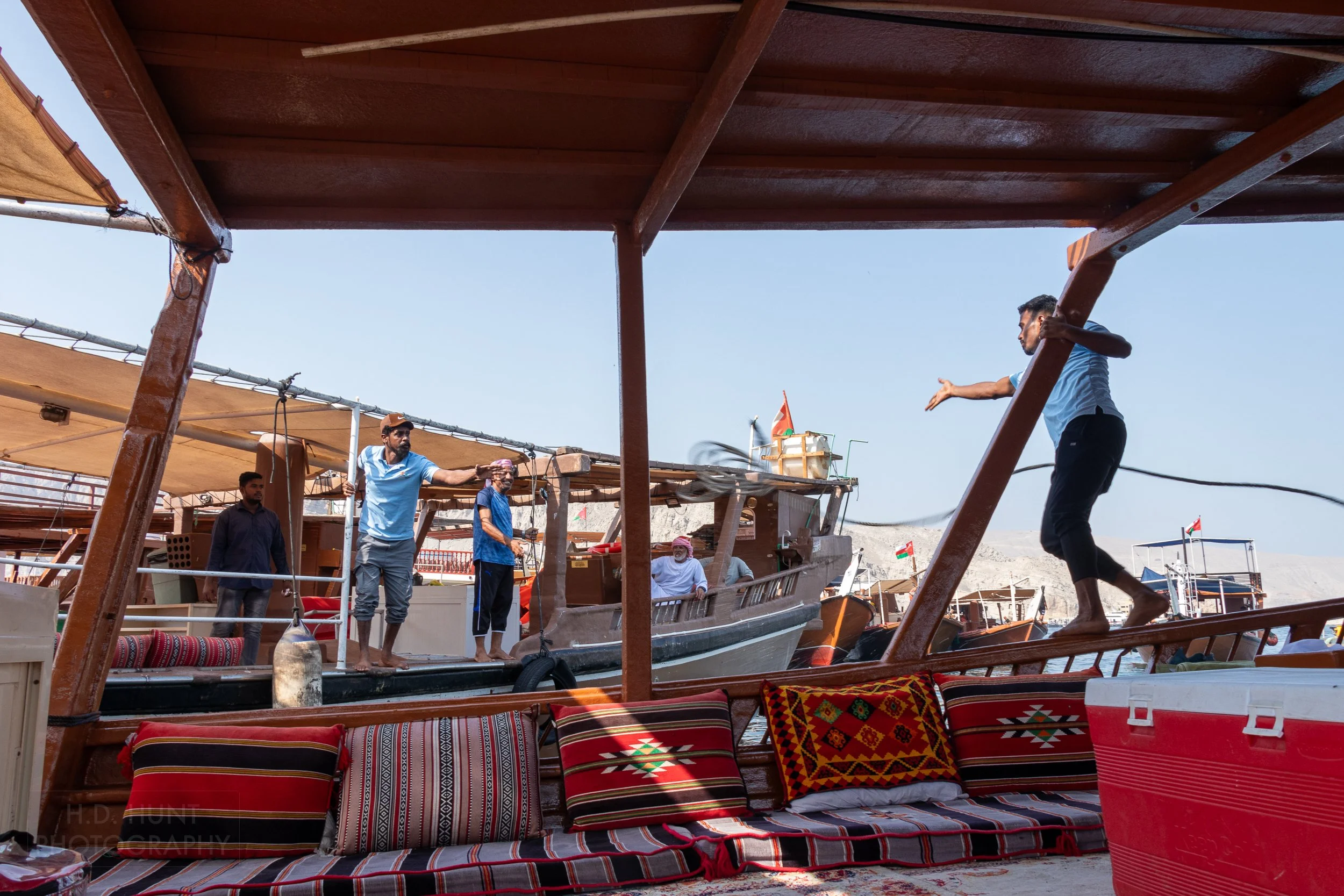 A man throws a rope from one dhow boat to an adjacent dhow boat in the Khasab Harbor, Oman.