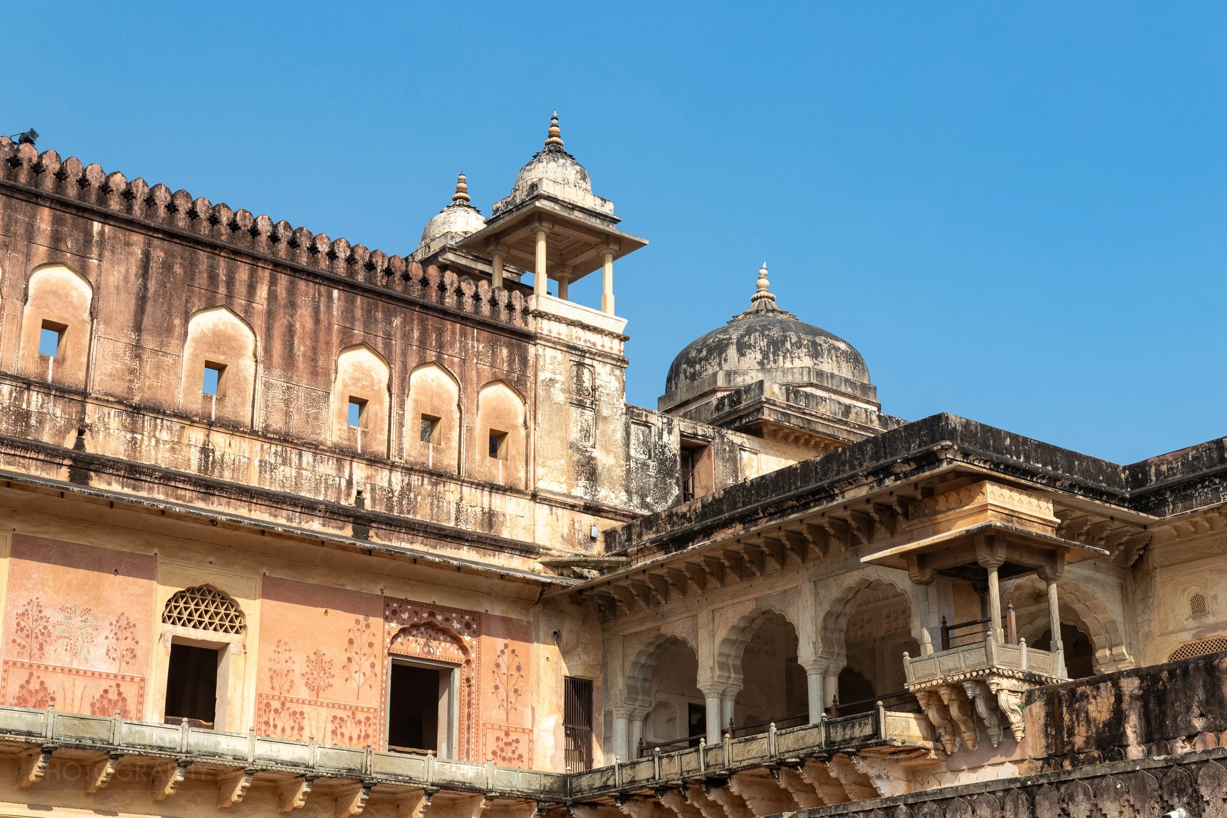 Yellow and black stone walls with a round cupola rise above a courtyard, Amber Fort, Amer, India.