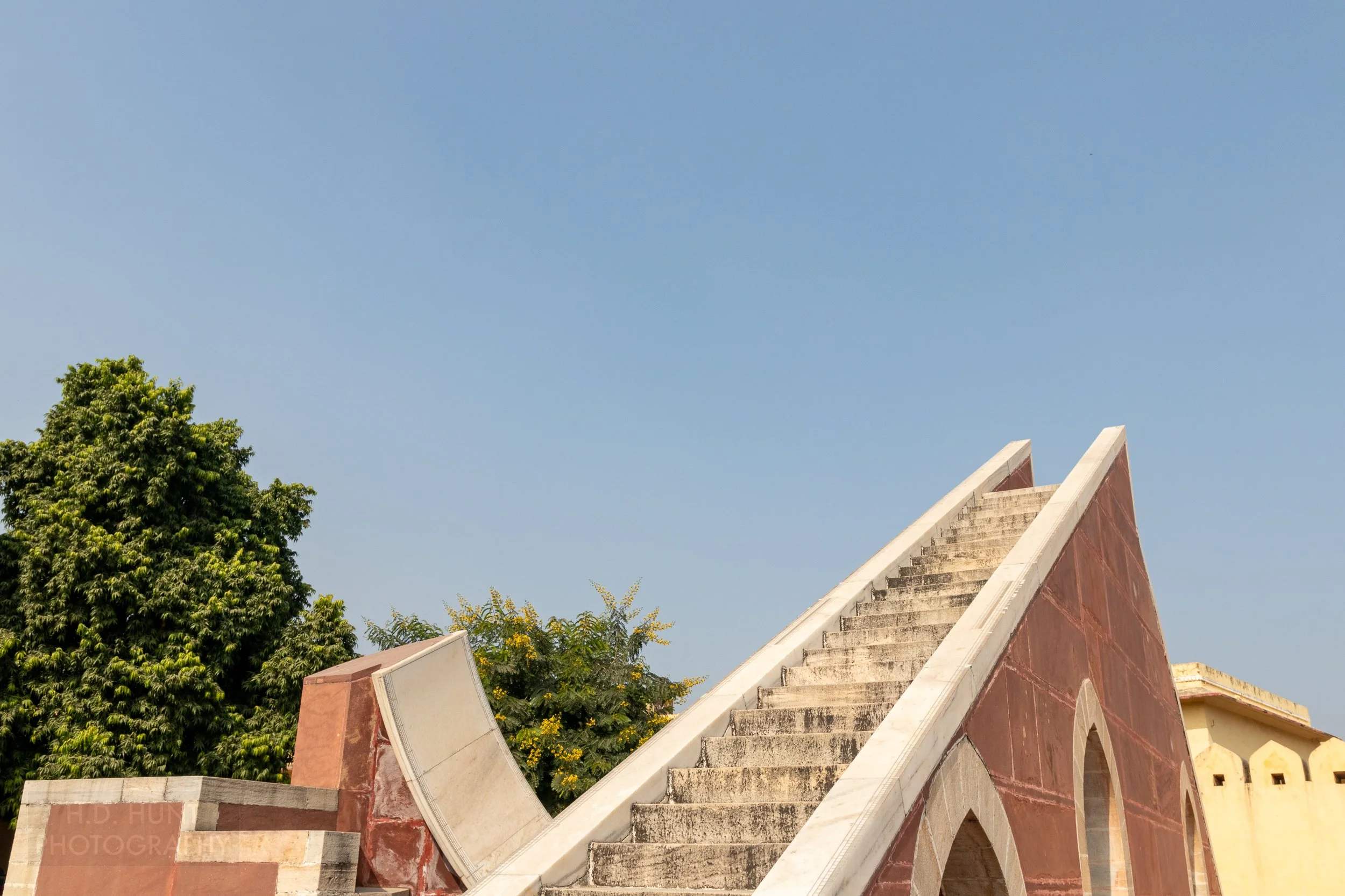 A large white stone staircase rises beside a white stone arc with black markings on its edges, Jantar Mantar, Jaipur, India.