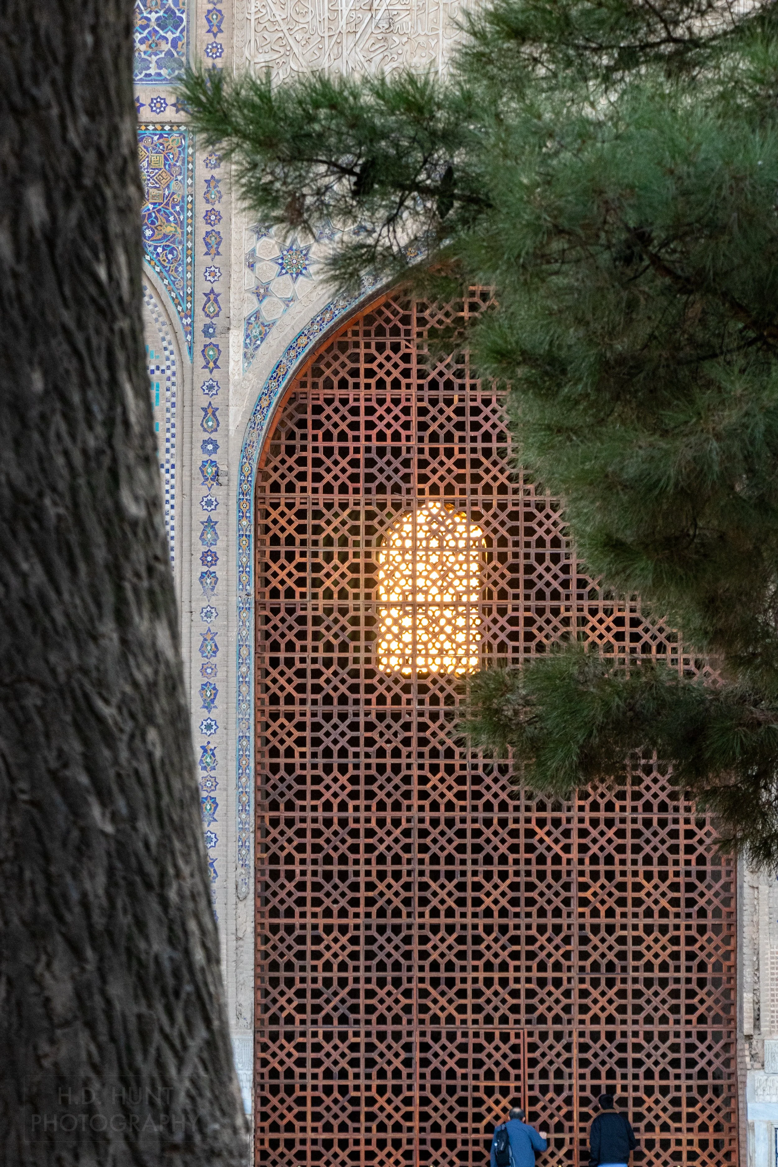 Two visitors peek through a large metal arched gate at the Bibi-Khanym Mosque, Samarkand, Uzbekistan.