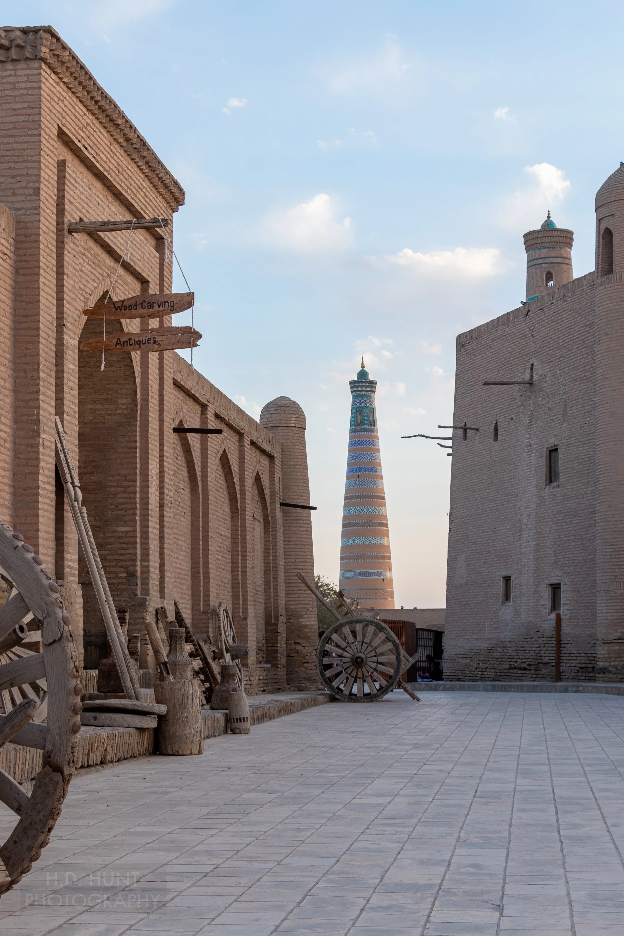 The tall Islam Khoja Minaret is seen behind a large-wheeled cart in an alleyway in Khiva, Uzbekistan.