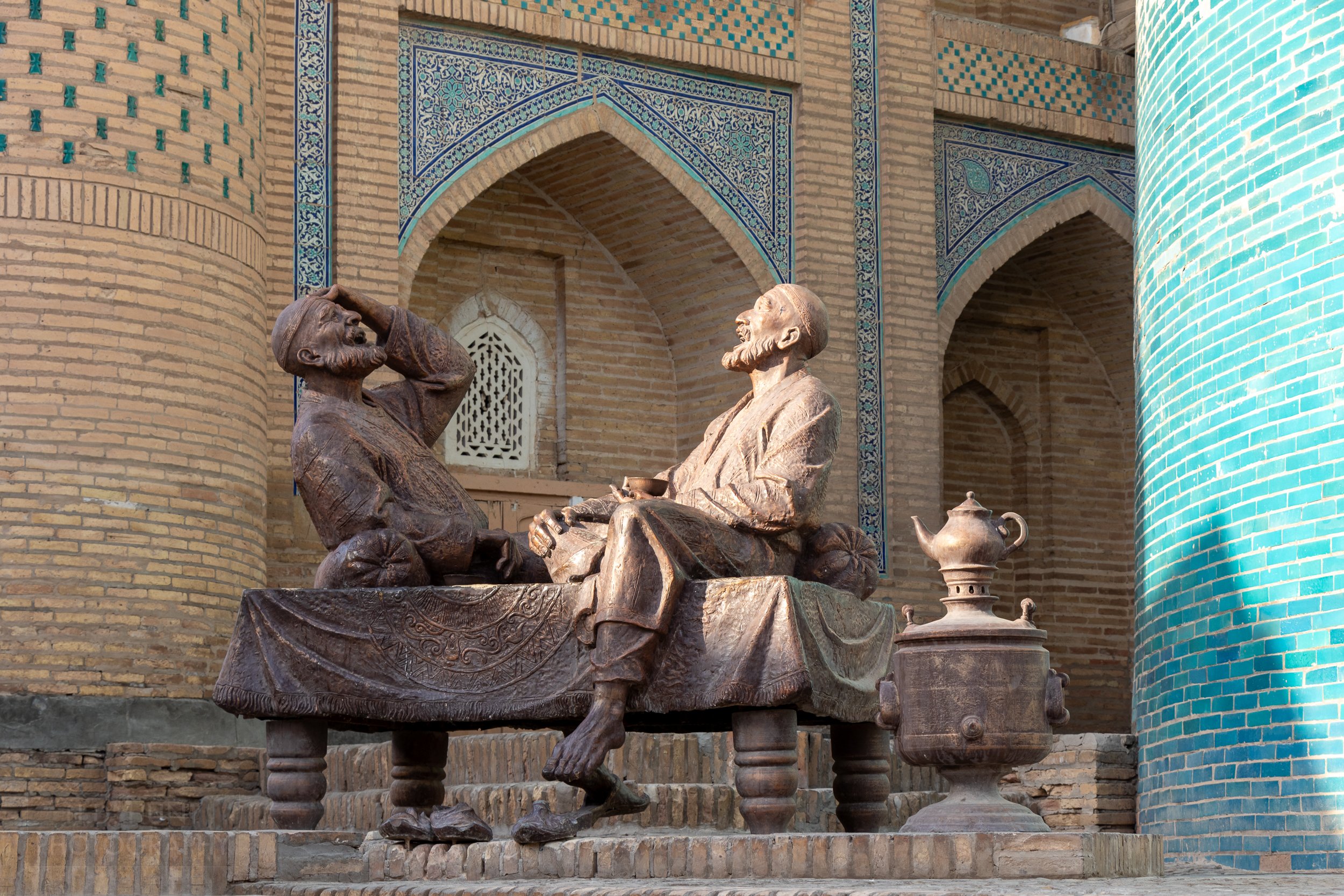 A metal statue of two men in traditional dress sitting on a bench laughing in Khiva, Uzbekistan.