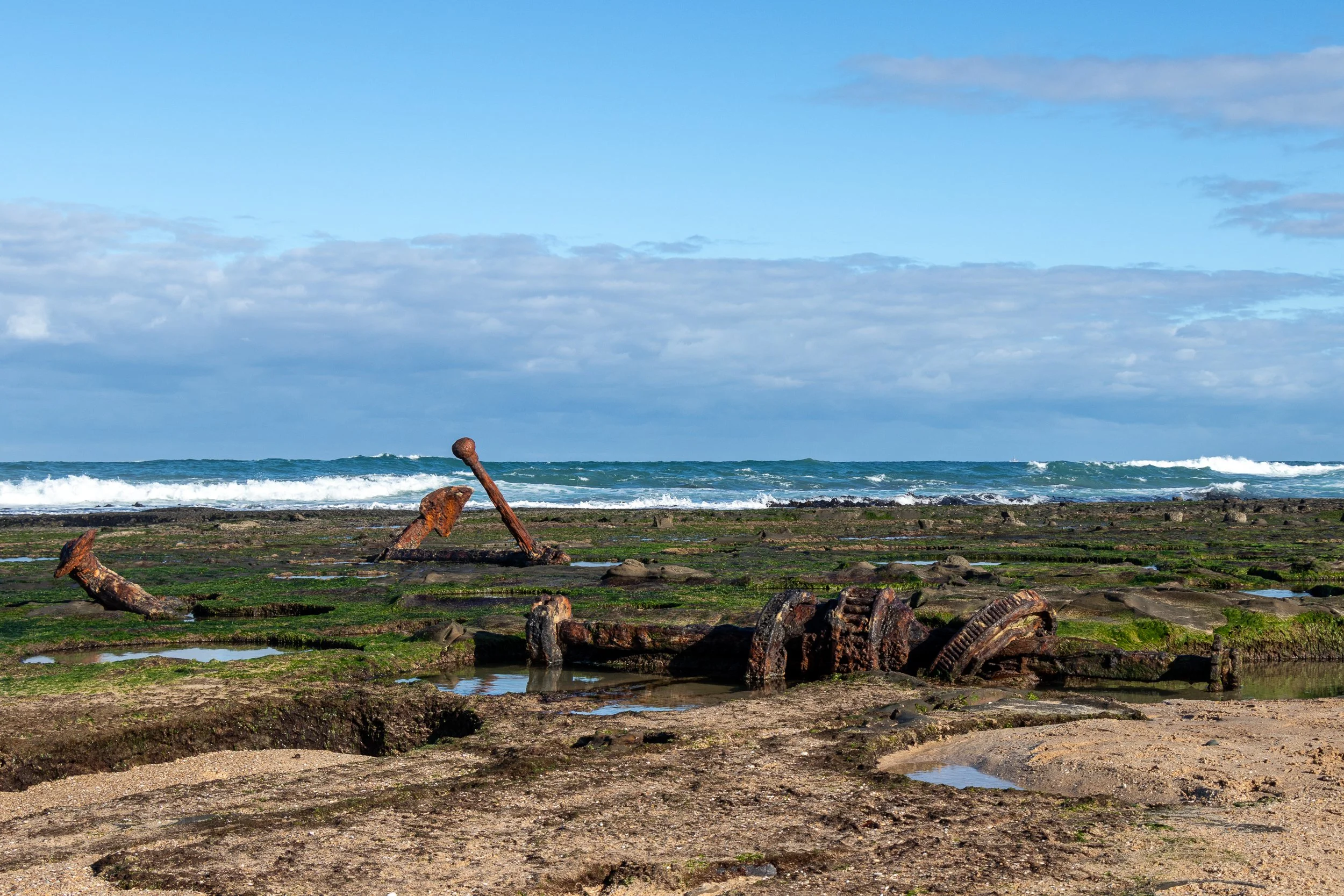 An anchor and various mechanical parts can be seen along a rock beach at Wreck Beach along The Great Ocean Walk, Victoria, Australia.