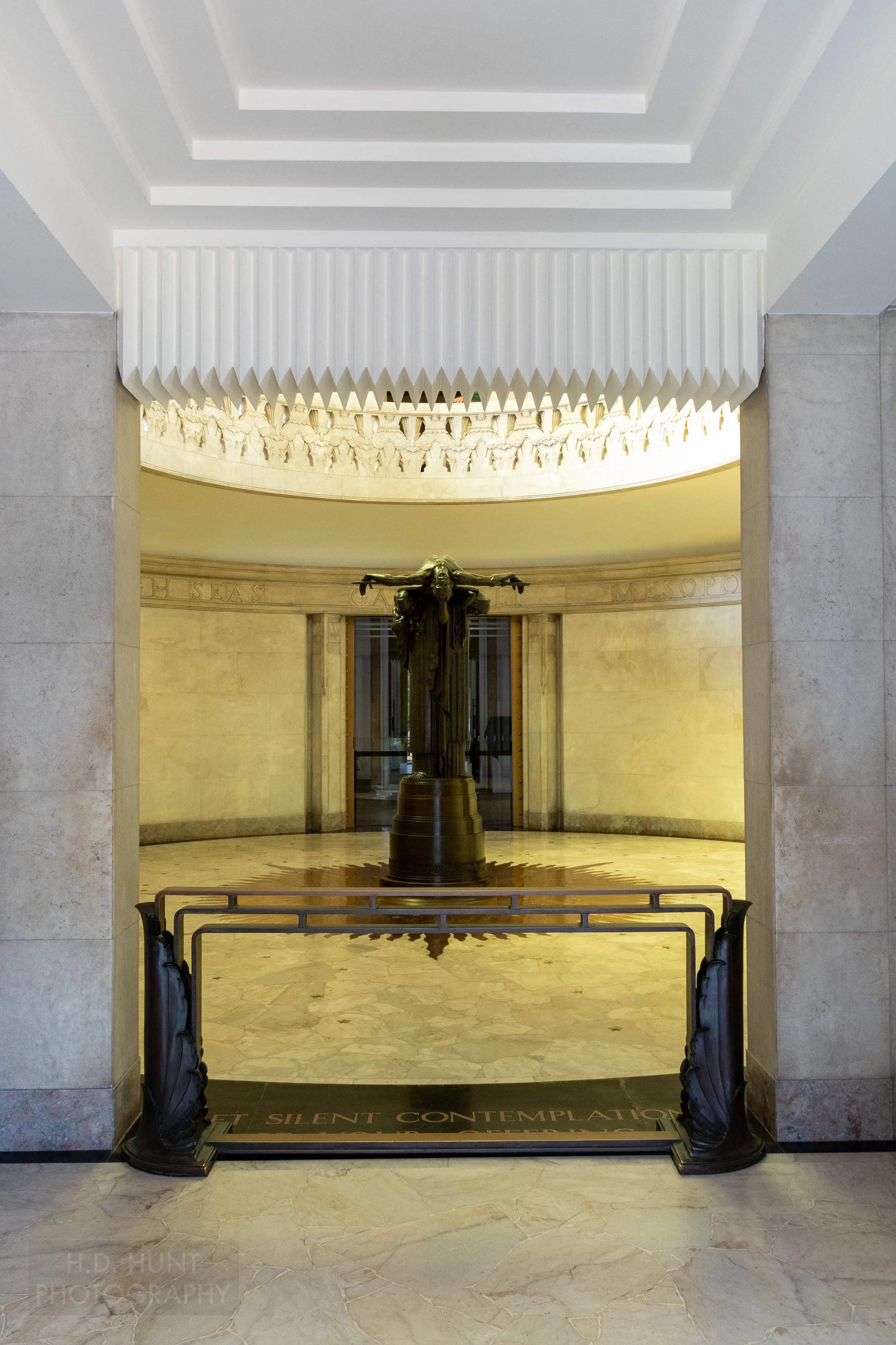 A dark-colored stone statue stands in the middle of a marble-lined circular memorial hall within the Anzac Memorial, Sydney, Australia.