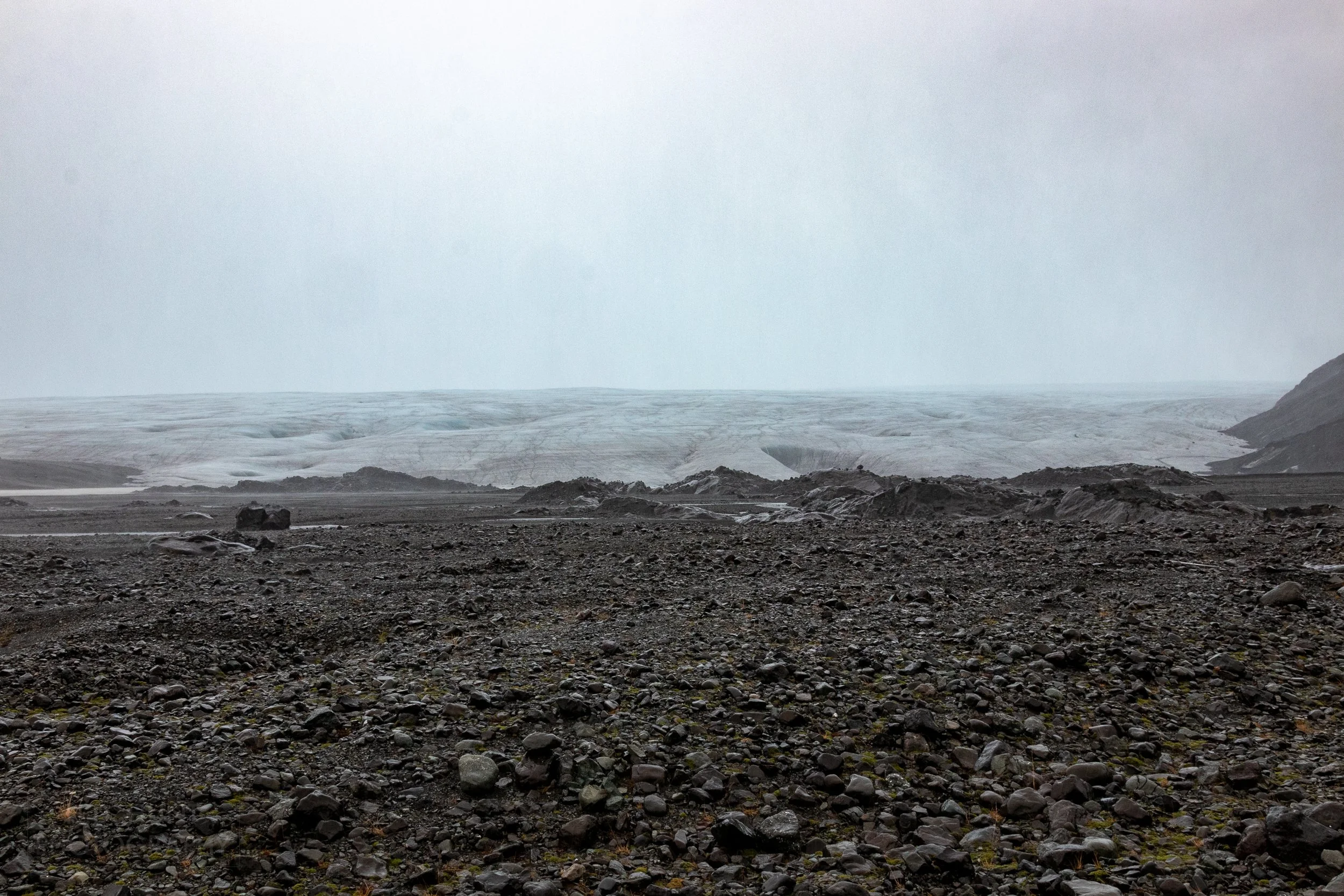 The edge of the Vatnajökull glacier sits atop a field of rocks and boulders beneath an incredibly hazy sky, Iceland.