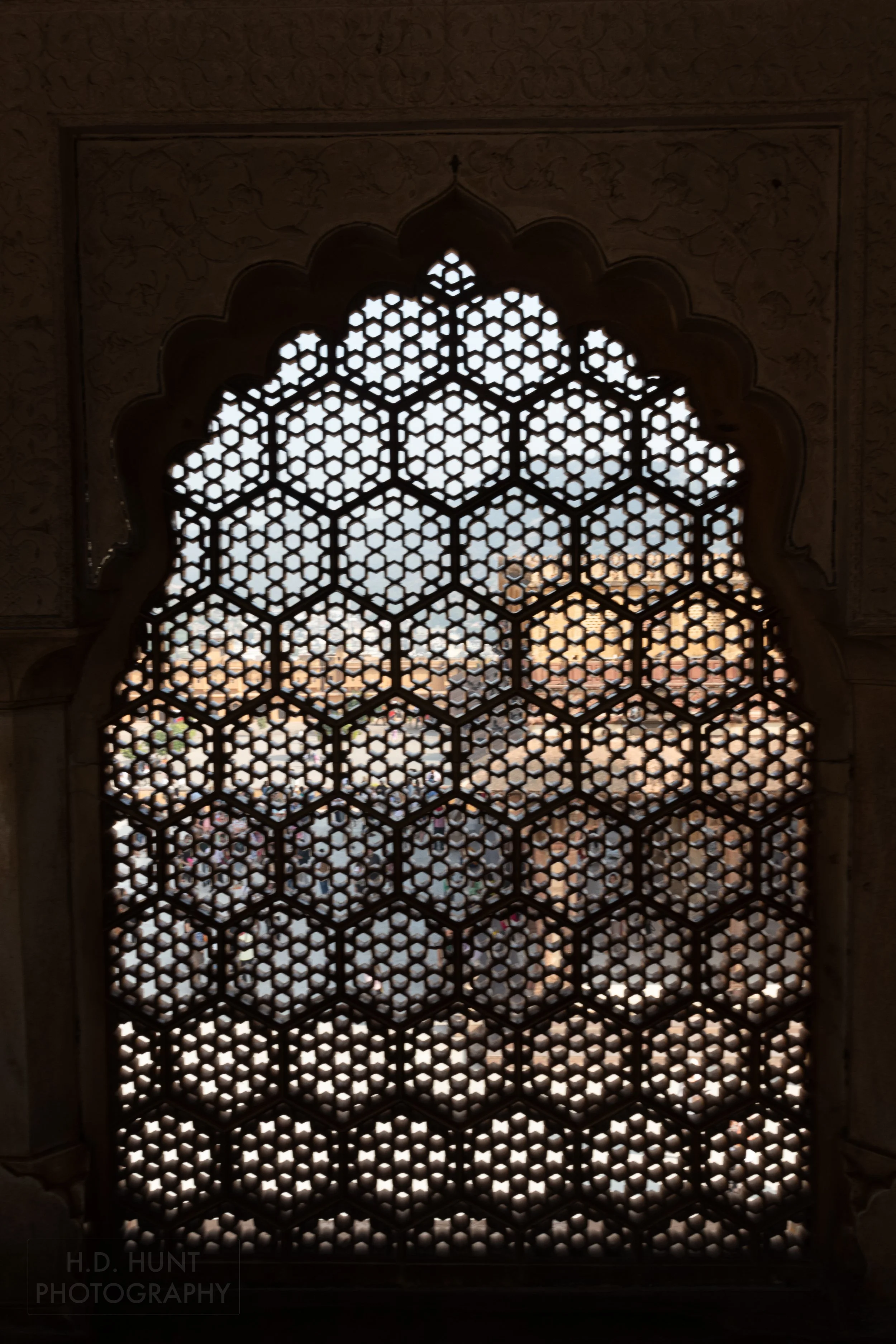 A yellow and pink structure is seen through a delicately carved stone window screen in Amber Fort, Amer, India.