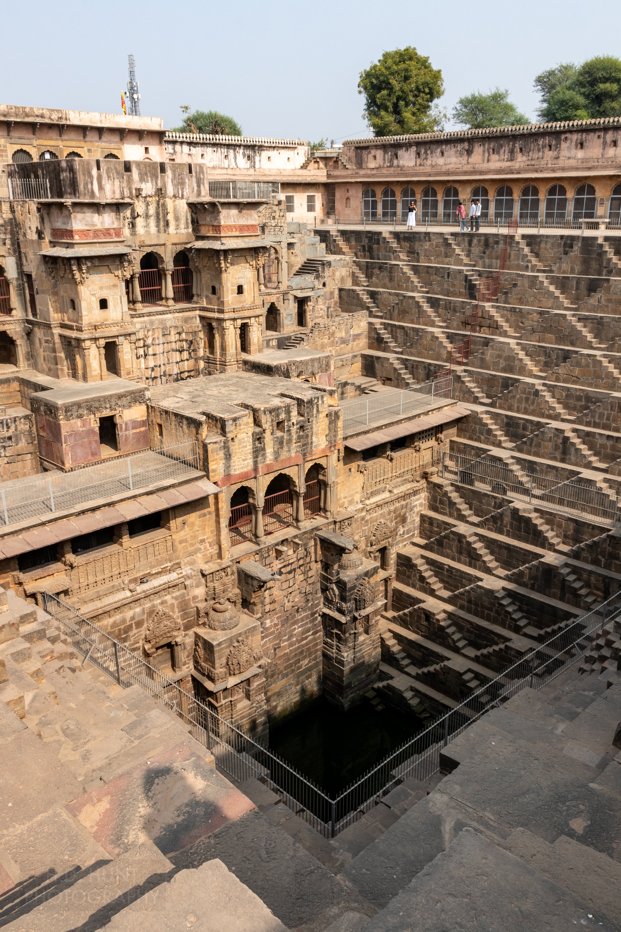 The zig-zag tan stone steps of Chand Baori rise from a small water well in the ground, Abhaneri, India.