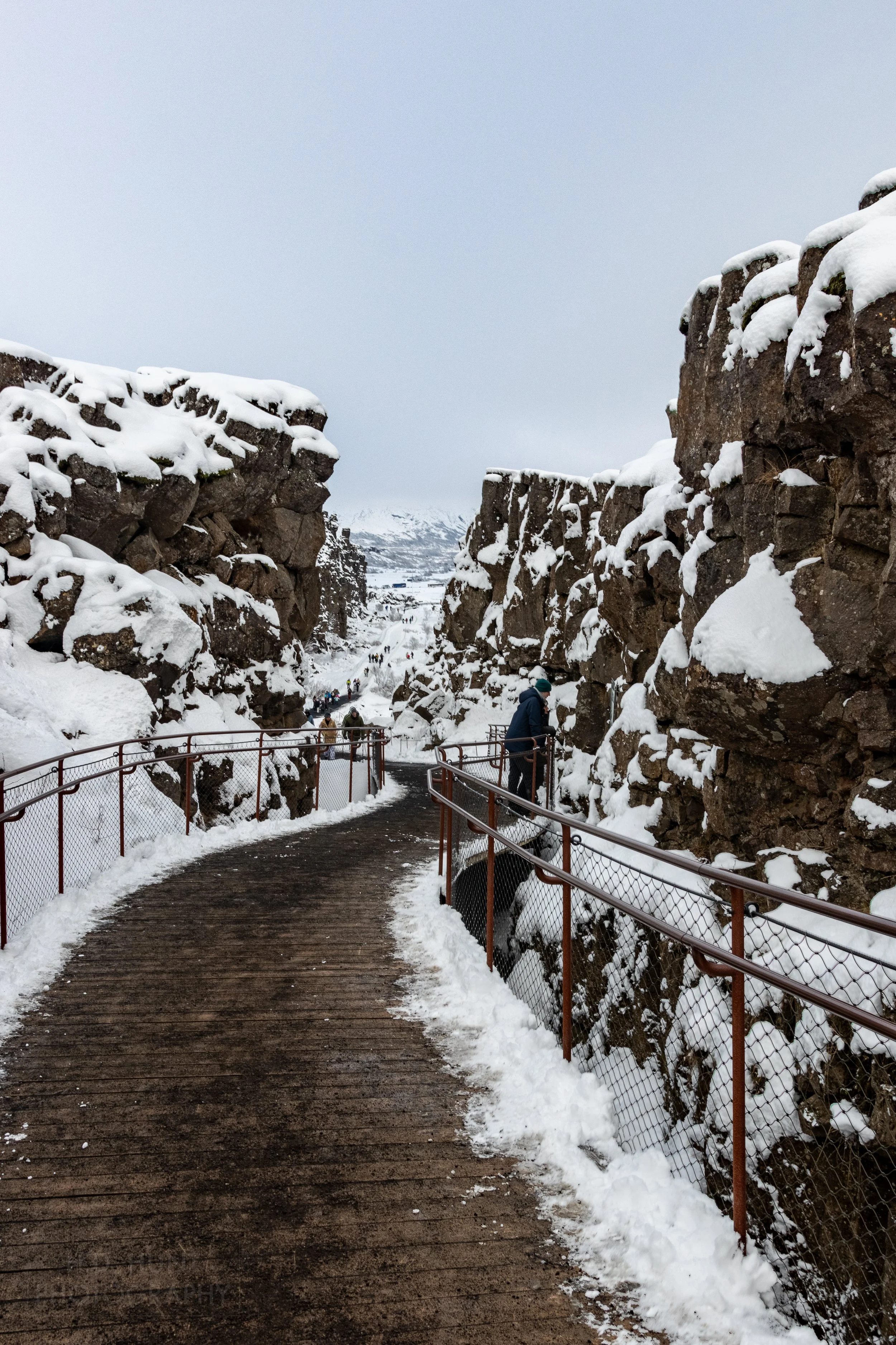 A long wooden boardwalk between two tall rock walls runs far into the distance at Þingvellir, Iceland.