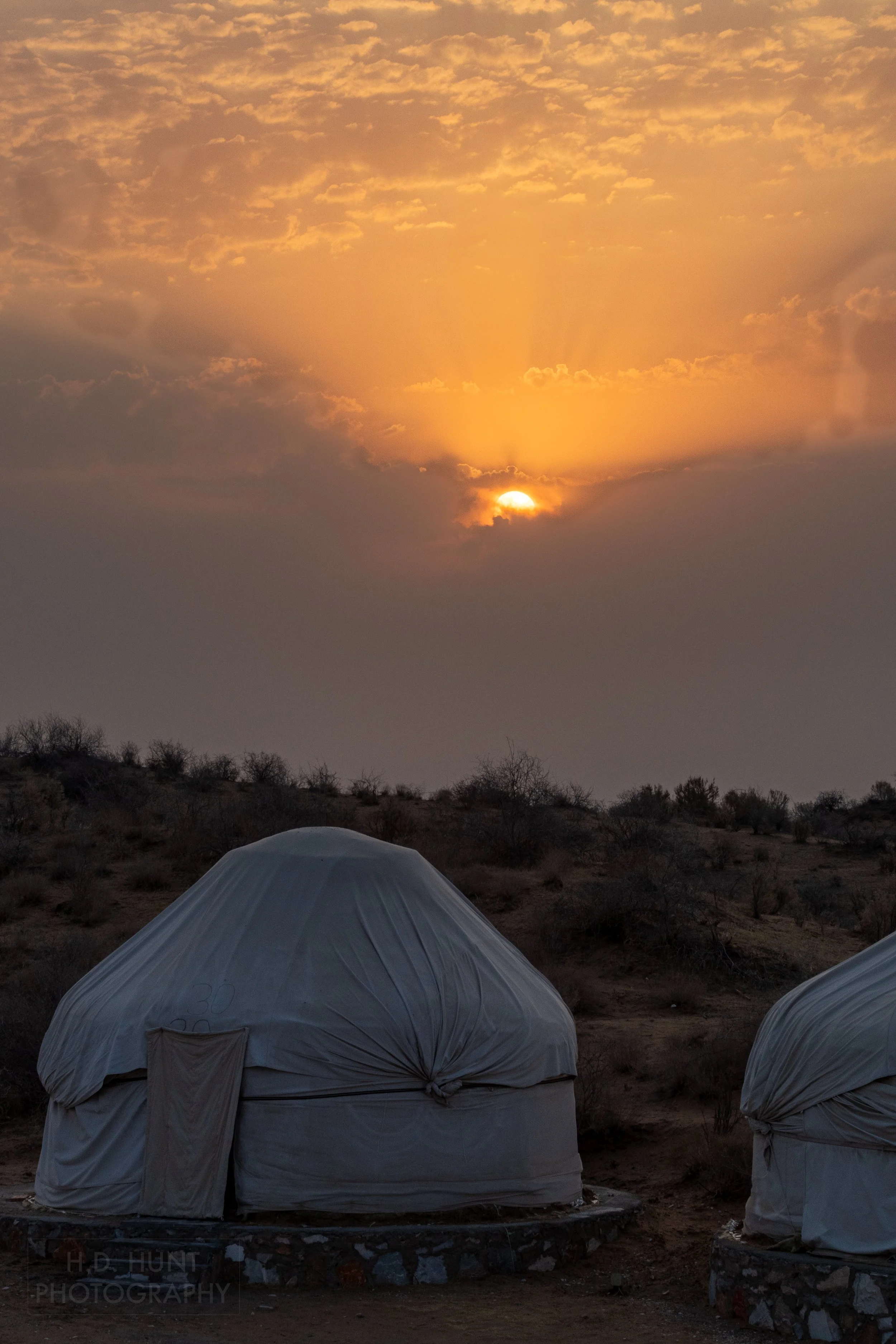 The sunrise peaks out from the clouds behind two yurts, Yangikazgan, Uzbekistan.