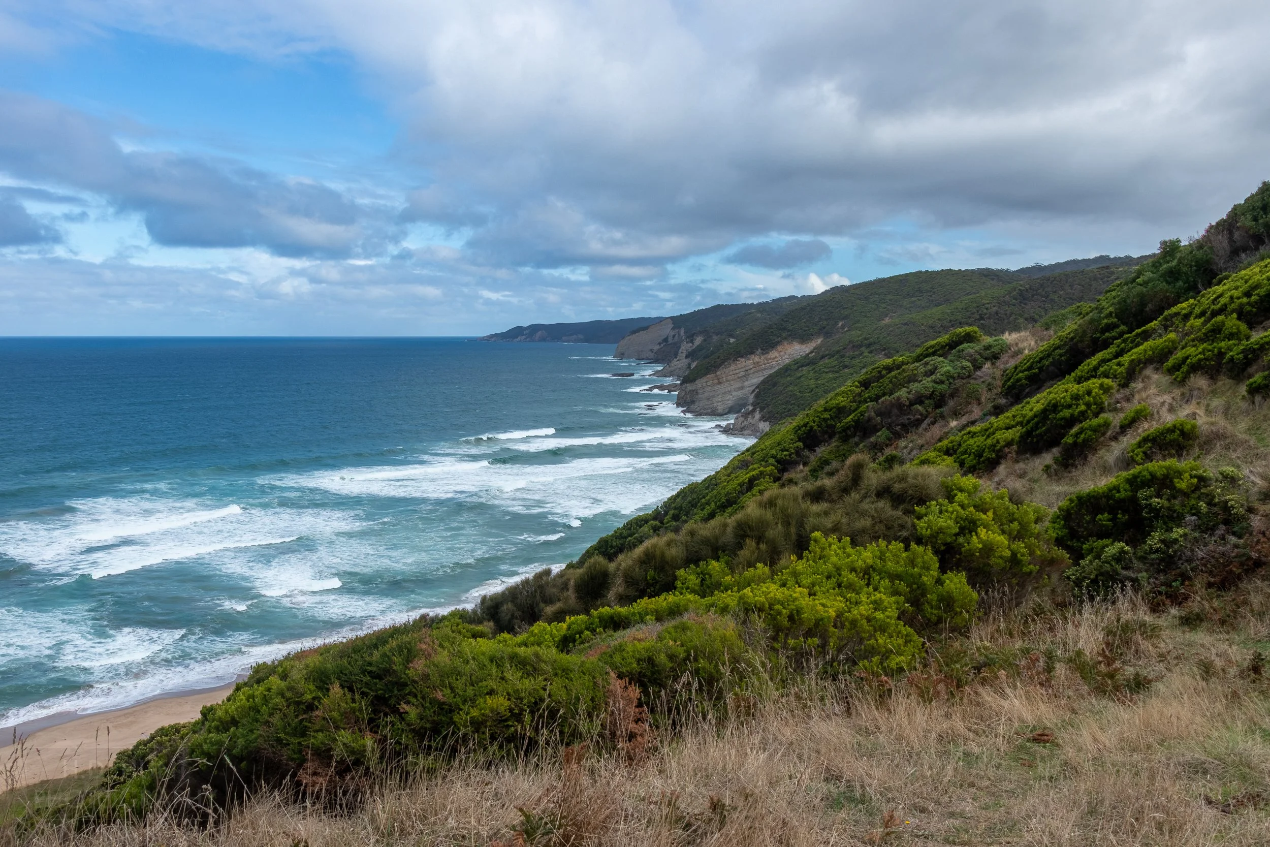 Waves crash against tall brown cliffs near The Great Ocean Walk, Victoria, Australia.