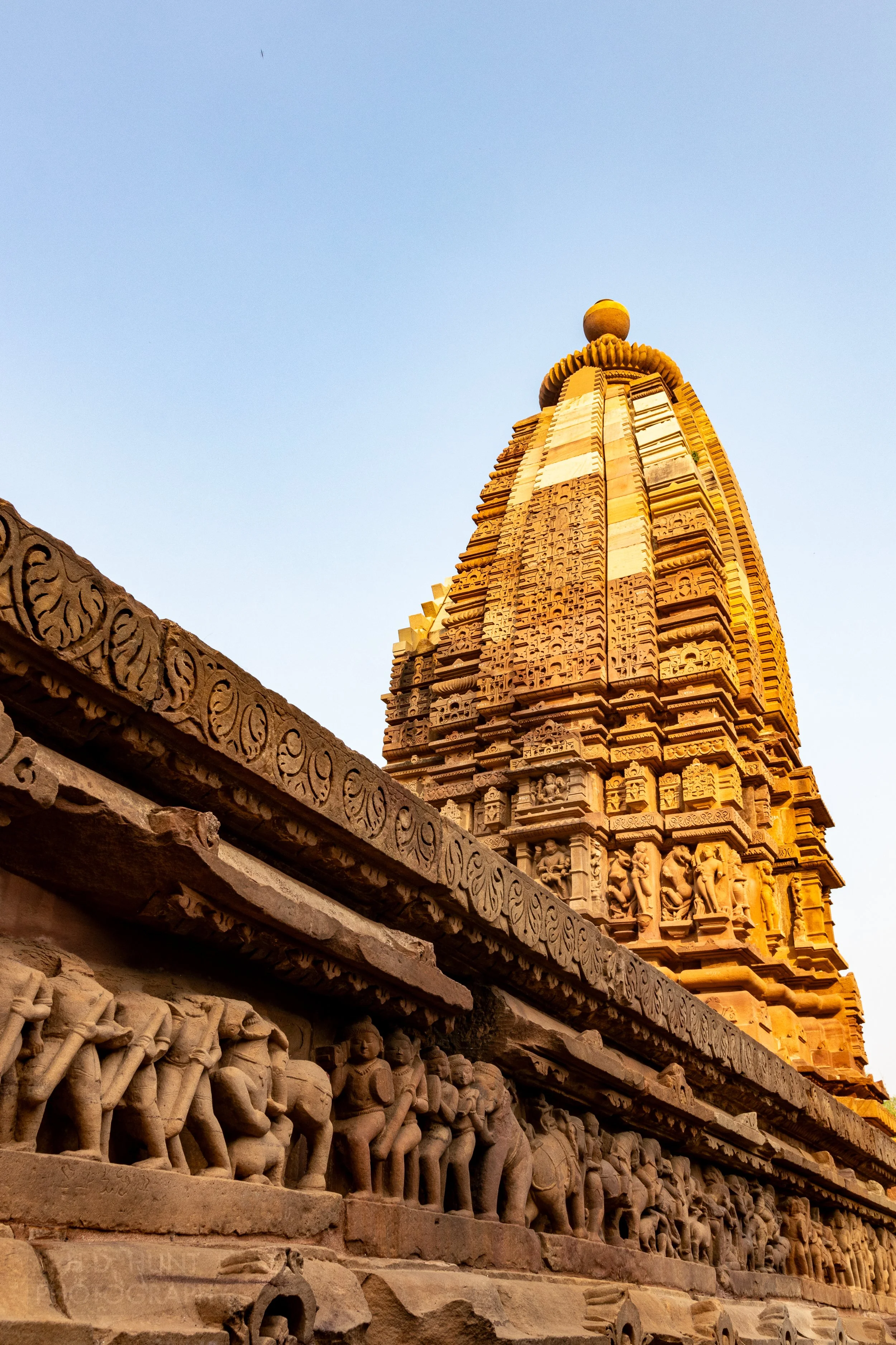 Close-up of the stone carvings adoring the Lakshmana Temple, Khajuraho Group of Monuments, India, with a tall temple tower rising in the background.