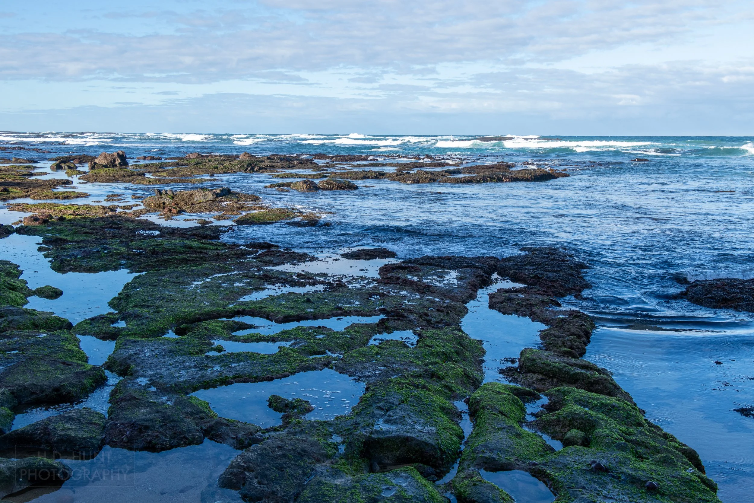 A rocky beach with small pools of water is seen beside the sea along The Great Ocean Walk, Victoria, Australia.