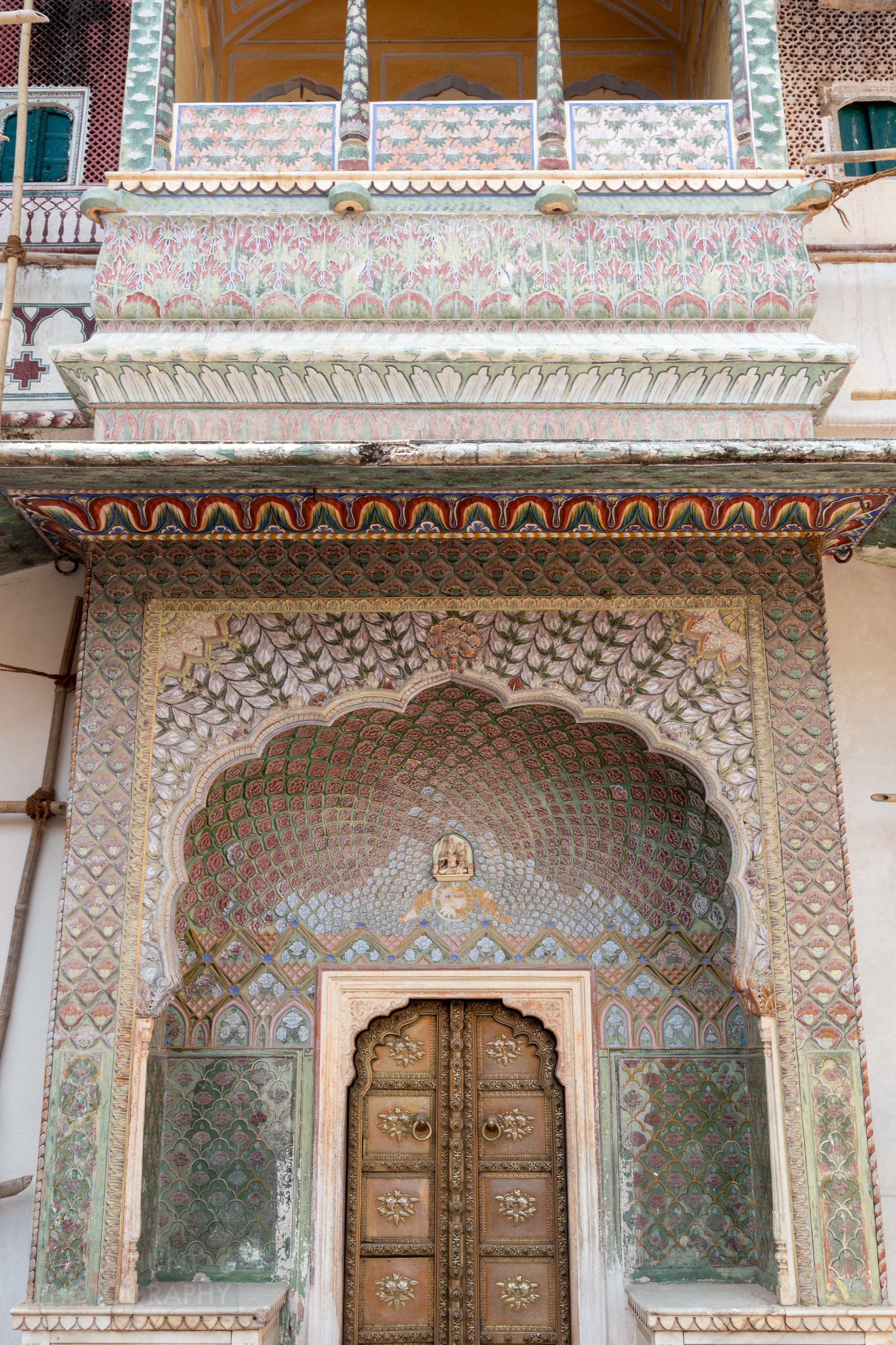 A door is surrounded by an archway adorned with multi-colored patterns, City Palace, Jaipur, India.