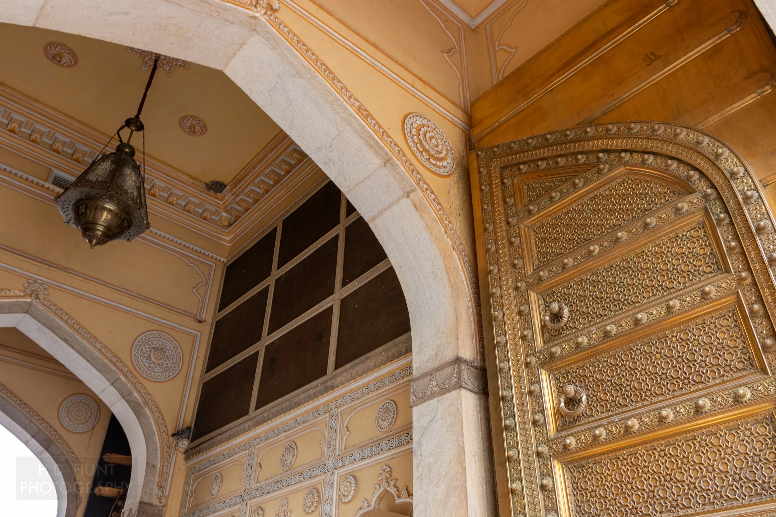 A golden door opens from an archway featuring a chandelier and yellow colored walls, City Palace, Jaipur, India.