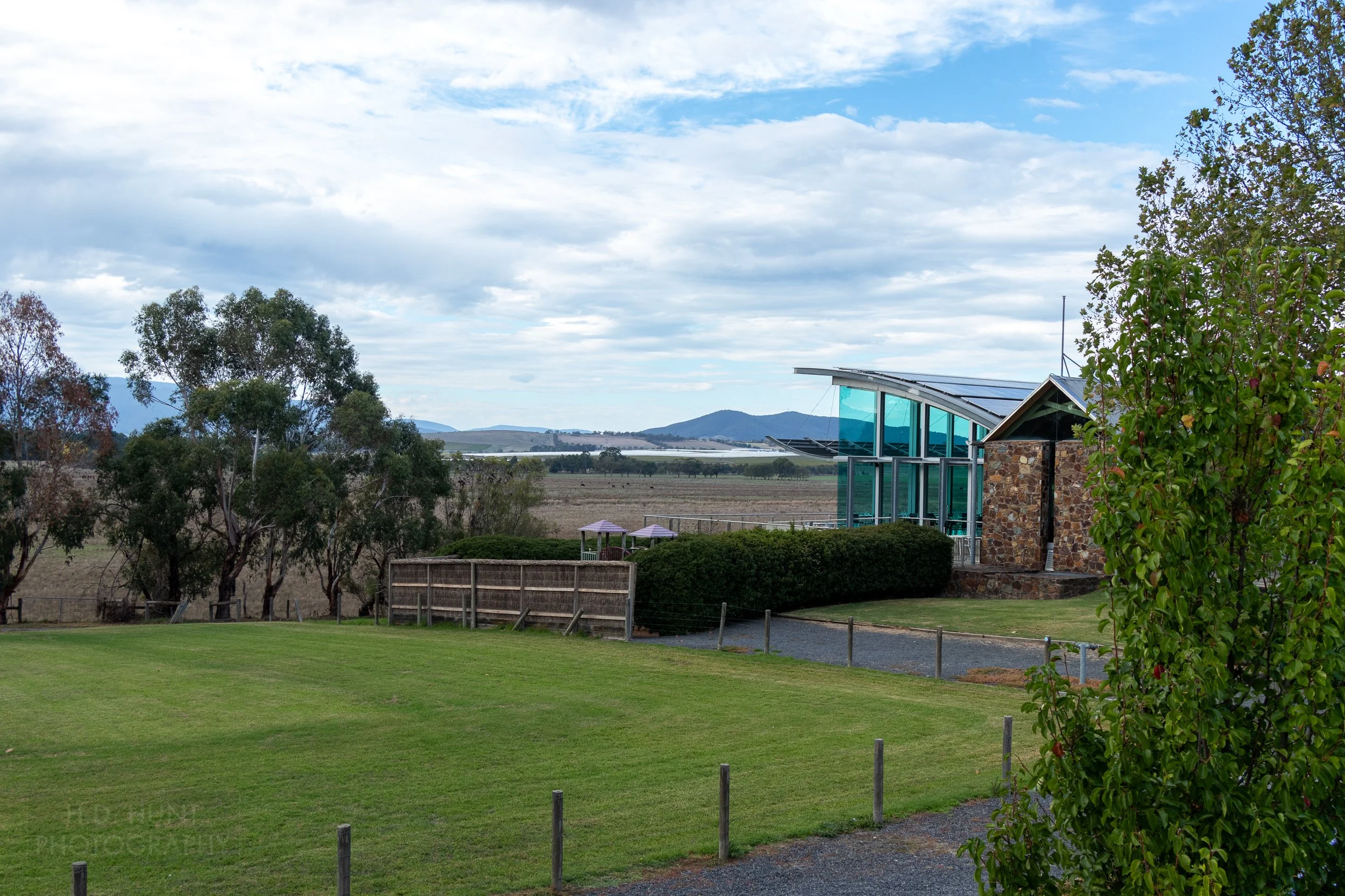 The green glassed-enclosed patio of the Yering Station Winery looks out towards a vineyard and manicured grass, Yarra Valley, Australia.