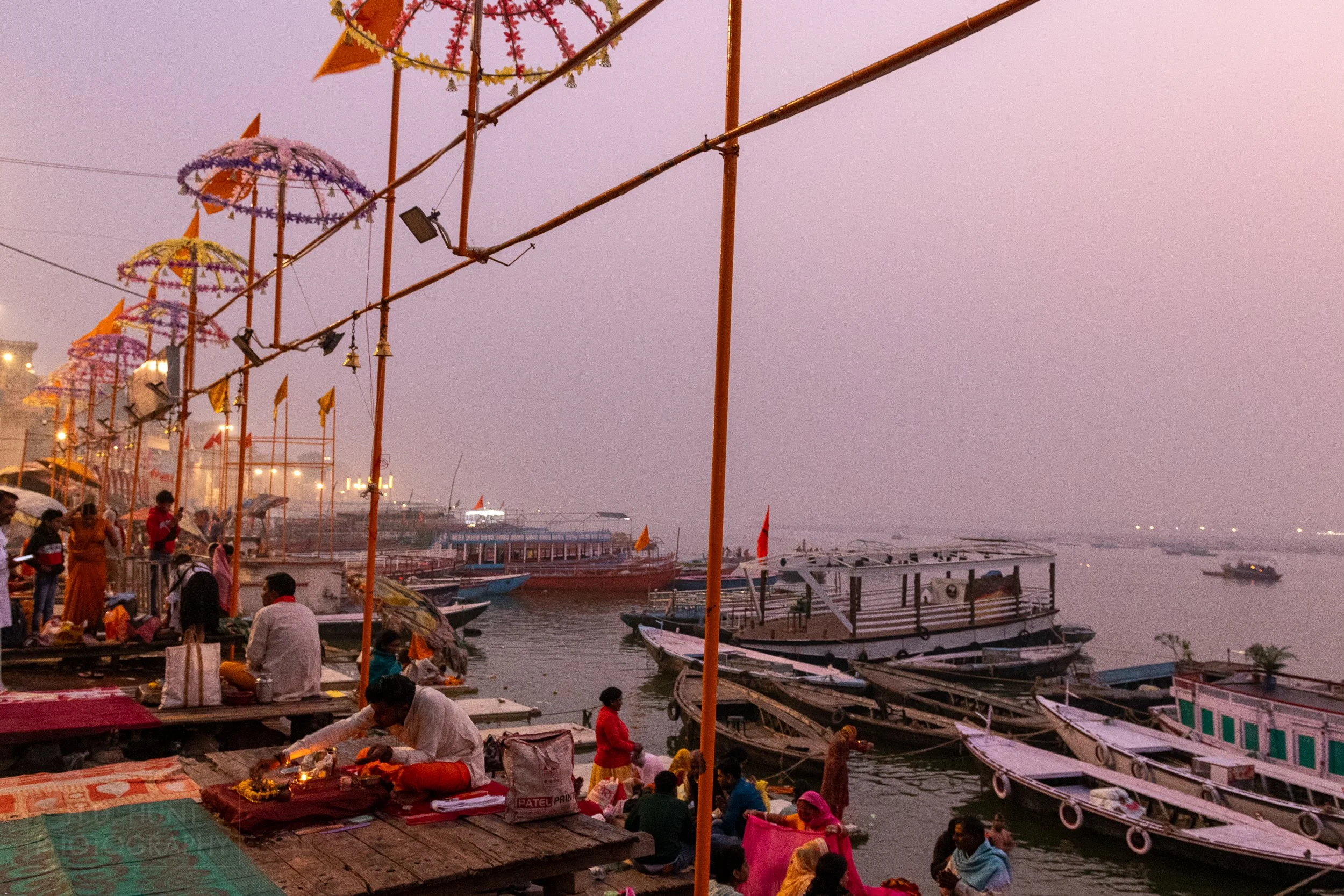Several boats congregate in the Ganges River while multiple worshipers gather riverside, Varanasi, India.