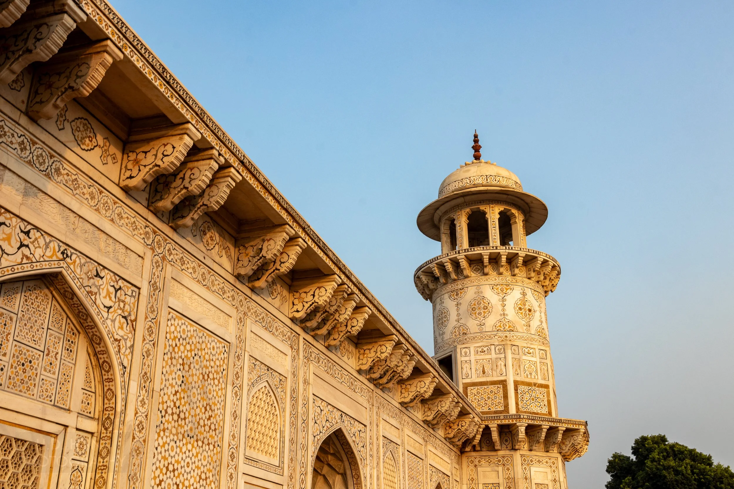 A tower and a detailed tile-covered wall are seen on the exterior of the Tomb of I’timad-ud-Daulah, Agra, India.