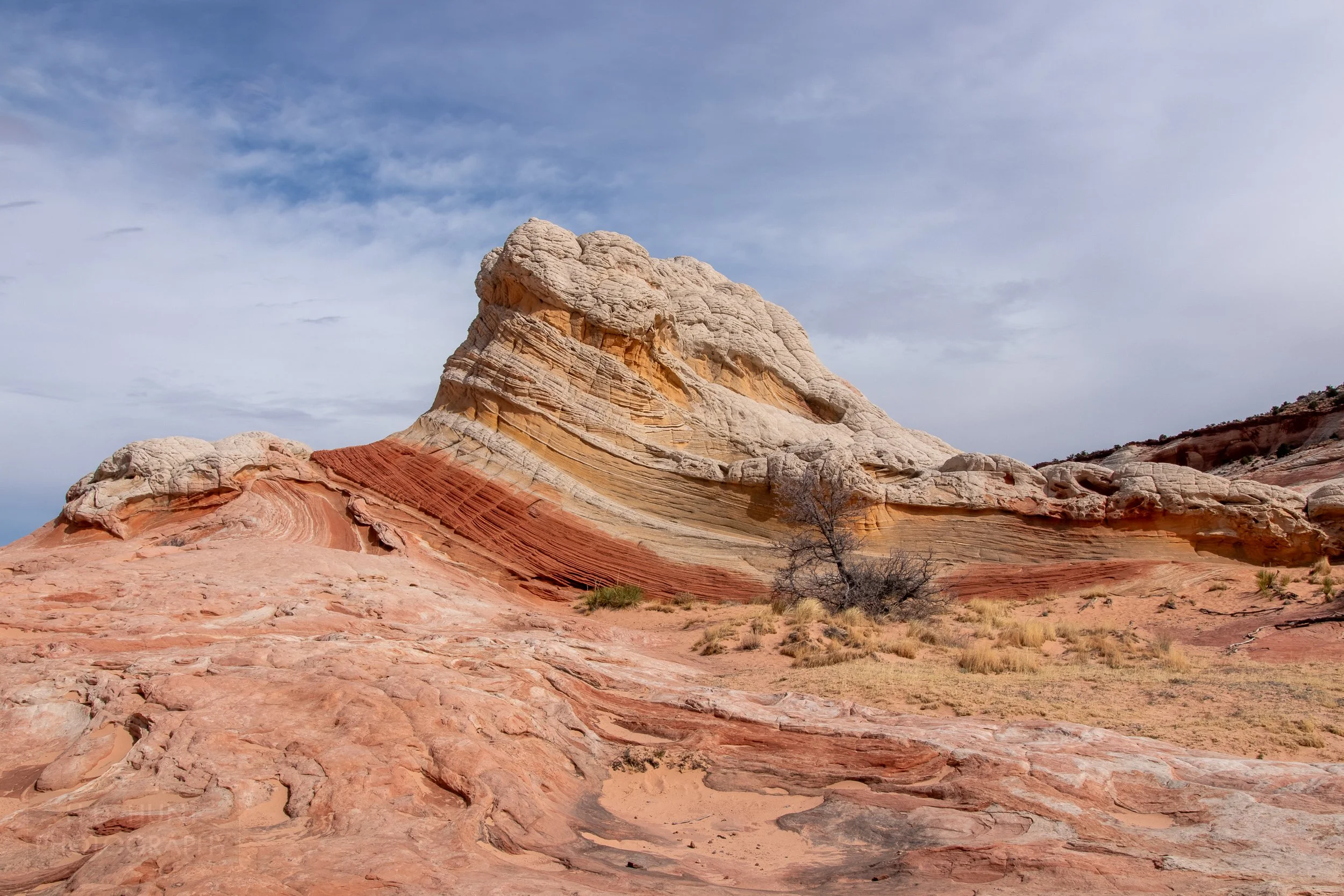 A large formation of white rock rises above a bedrock of red, white, and tan striped sandstone in White Pocket, Vermillion Cliffs National Monument, Arizona, United States.