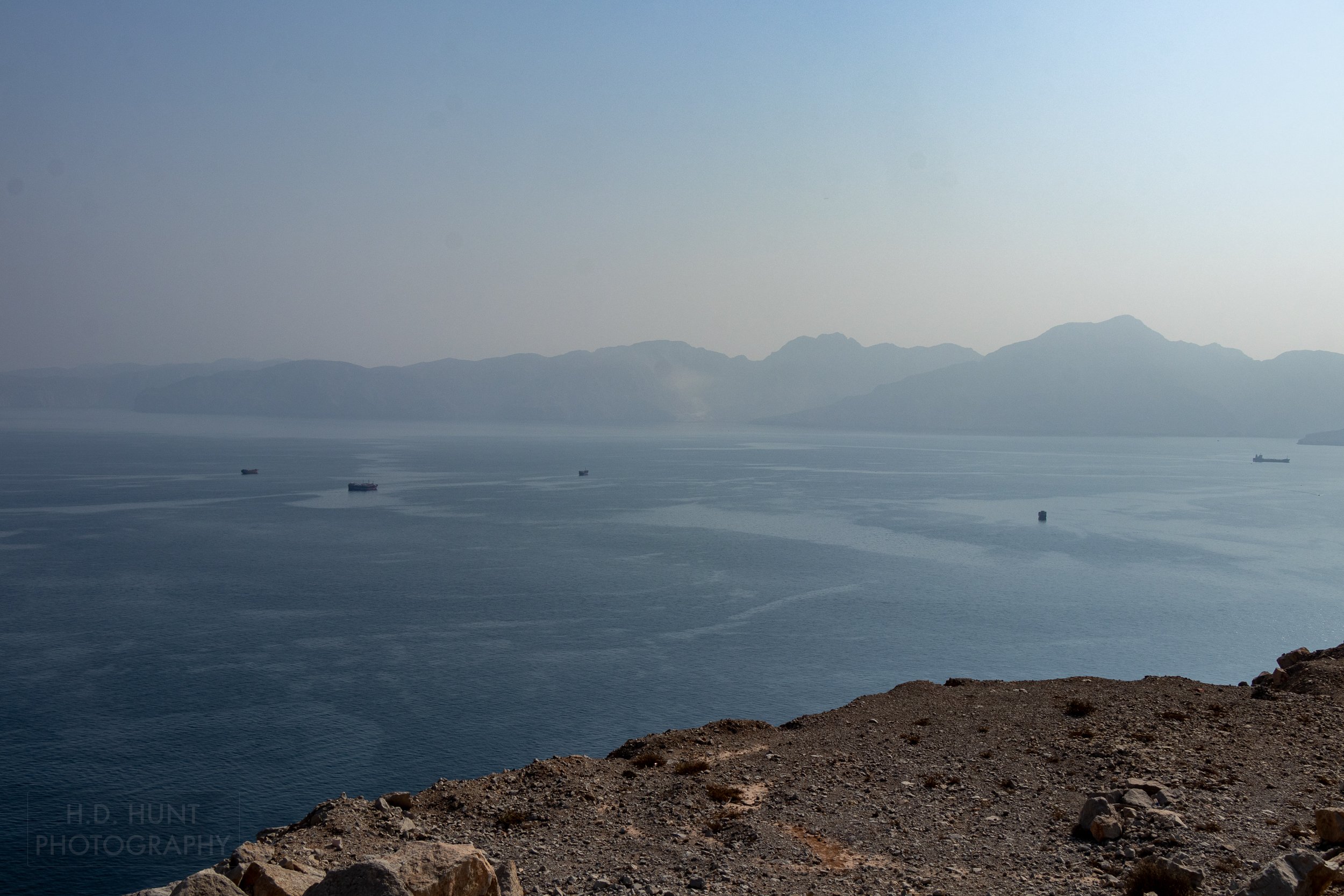 Ships sit in the Strait of Hormuz with the mountains of the Musandam Peninsula in the background.