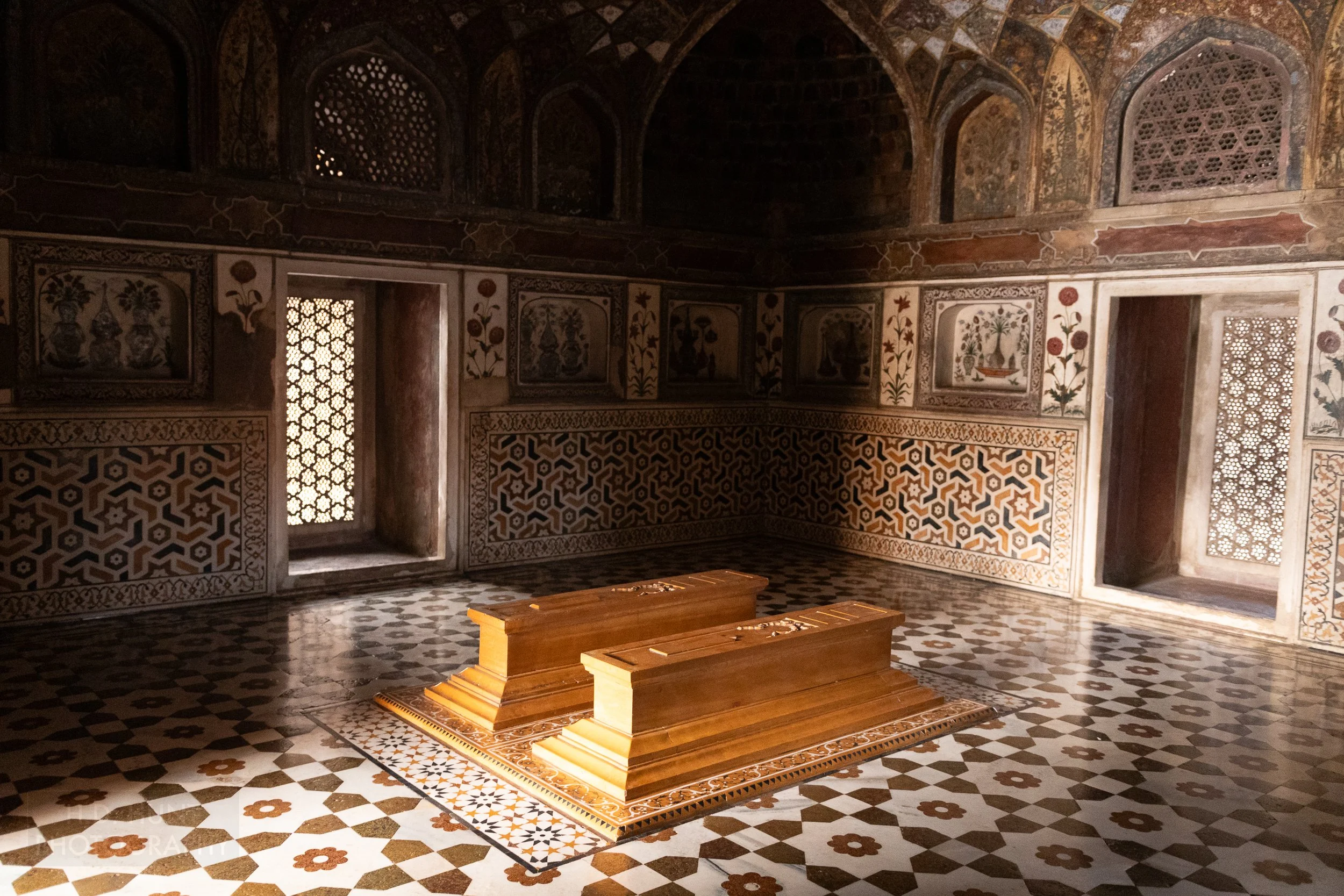 Two cenotaphs lie on the floor of a room with detailed tiles of geometric shapes on the floor and walls in the Tomb of I’timad-ud-Daulah, Agra, India.