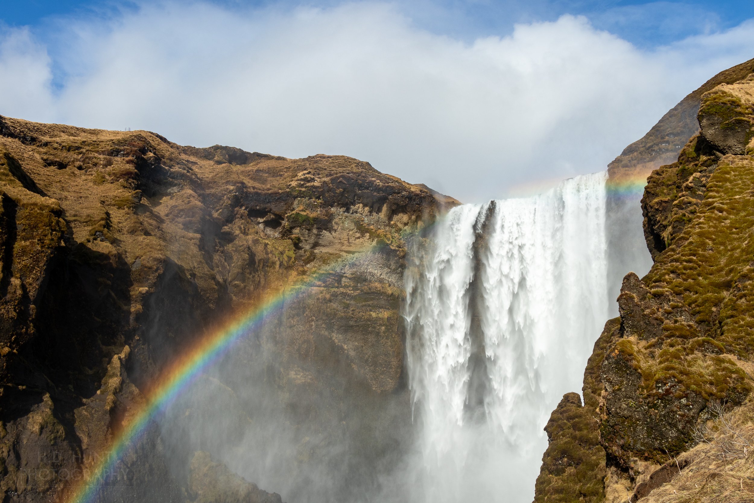 The water of Skógafoss spills over tall brown cliffs, forming a rainbow, Skógafoss, Iceland.