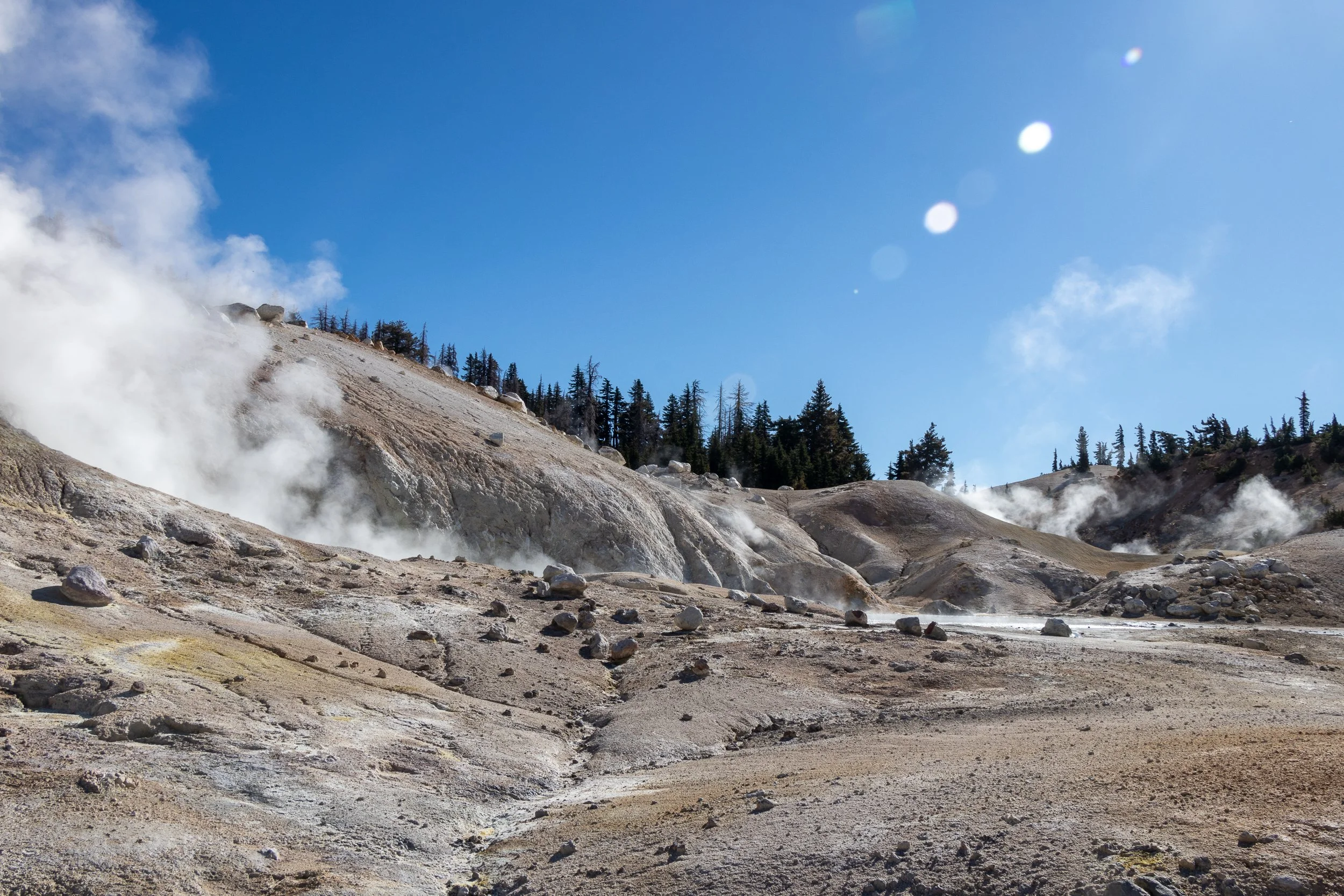 Steam rises from multiple locations on a tan and white landscape, Bumpass Hell, Lassen Volcanic National Park, California, United States.