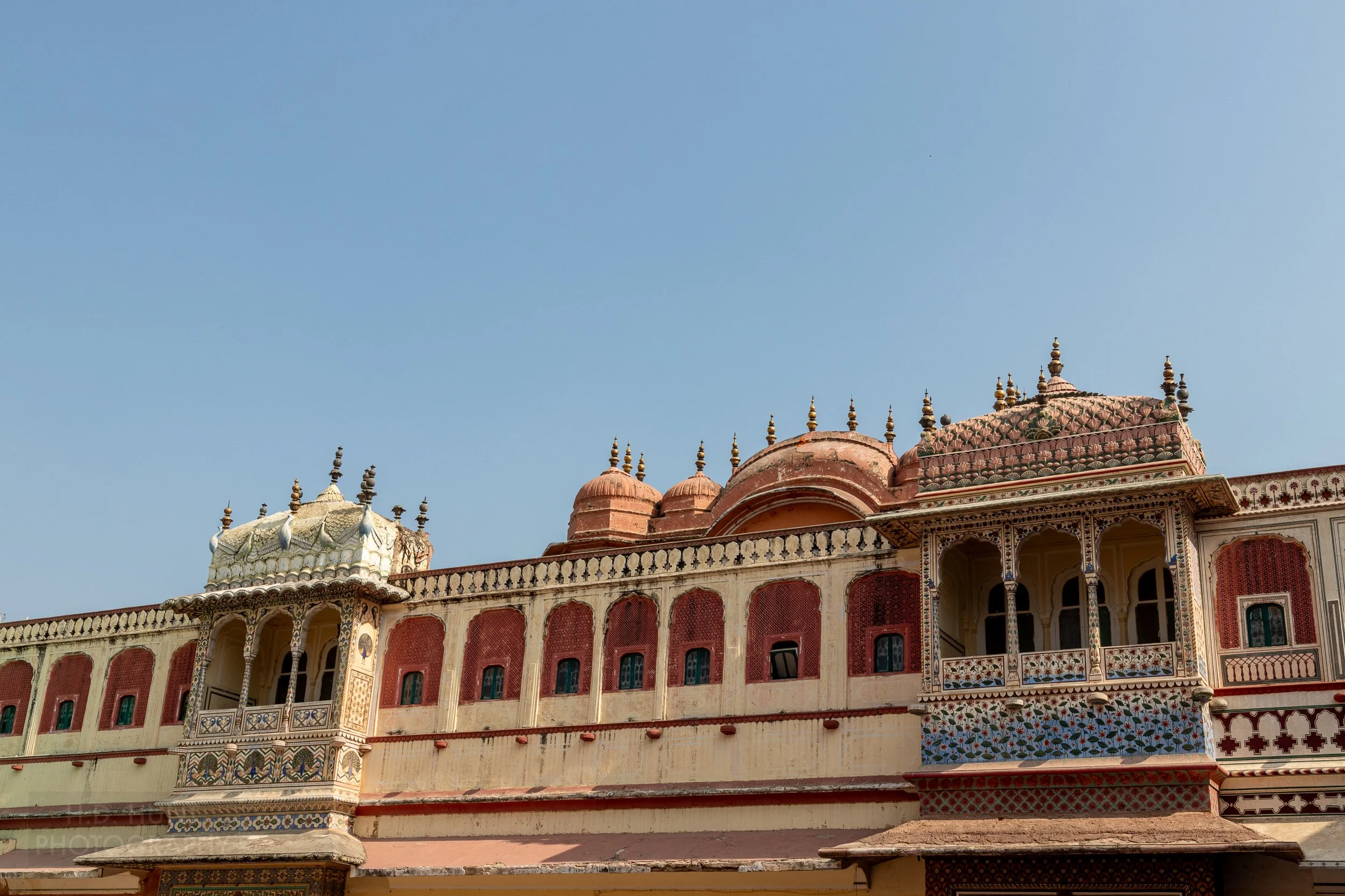 A long wall with two large balconies covered with colorful paint and tiles, City Palace, Jaipur, India.
