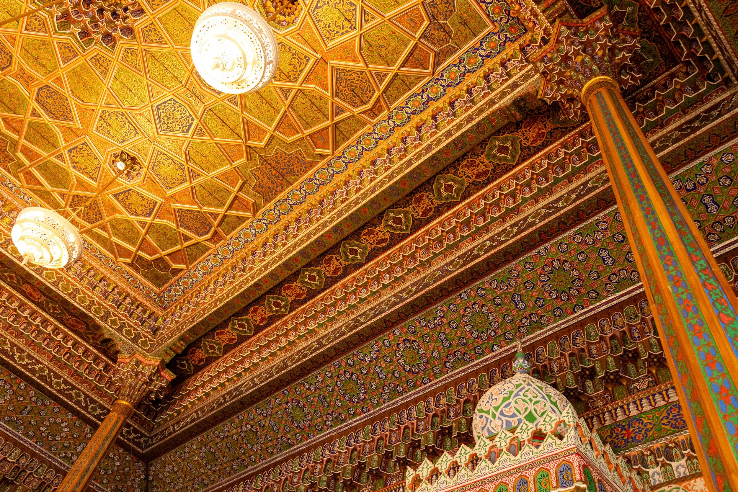 Chandeliers hang from an intricately designed ceiling featuring a gold finish and muqarnas at the Museum of Applied Arts, Tashkent, Uzbekistan.