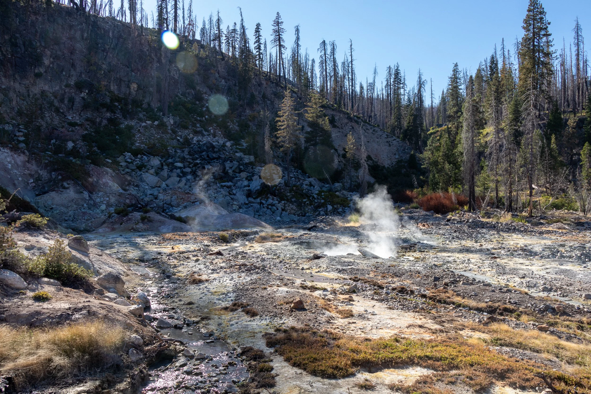 Small puffs of steam rise from a barren landscape of mud and rock, Devils Kitchen, Lassen Volcanic National Park, California, United States.
