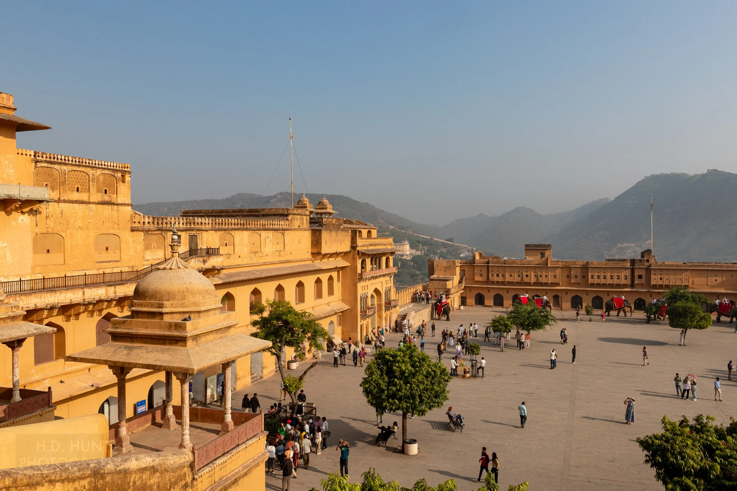A large courtyard is seen besides a bright yellow stone building at Amber Fort, Amer, India.